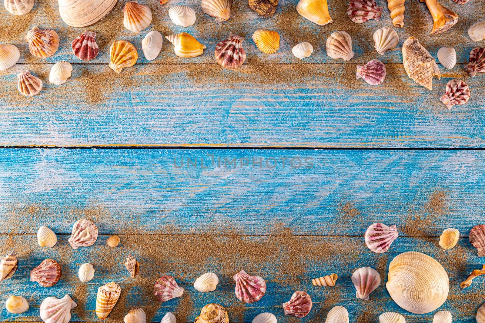 Summer time concept with sea shells on a blue wooden background and sand. Seashells frame on wooden background nautical border. Focus on seashells.