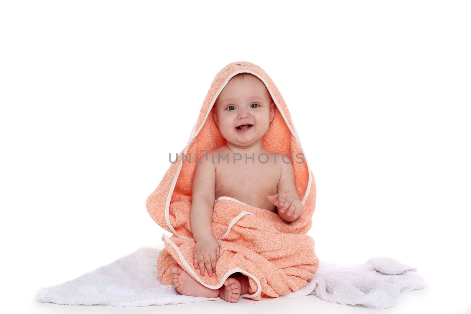 Sweet small baby covered with an orange towel, sits on a plaid on a white background. Cute infant after bath. Eight months