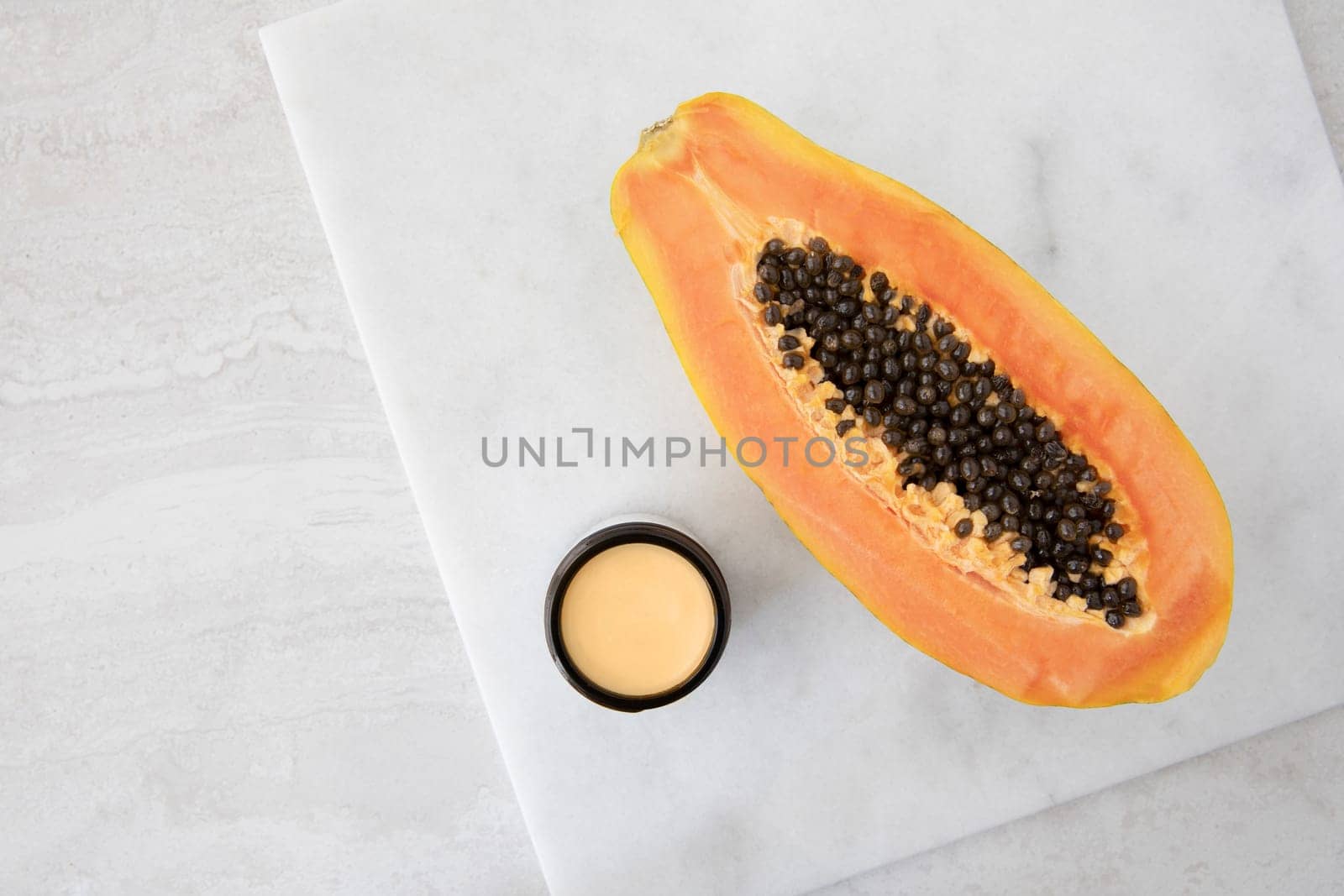 Half a papaya on a marble surface with small jare of papaya extract cream.