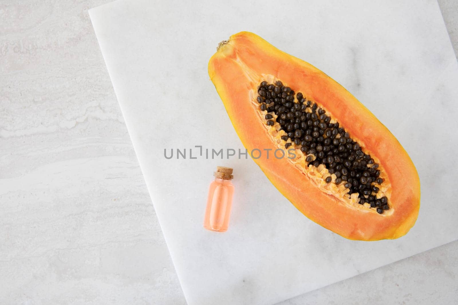 Half a papaya on a marble surface with small bottles of papaya extract.