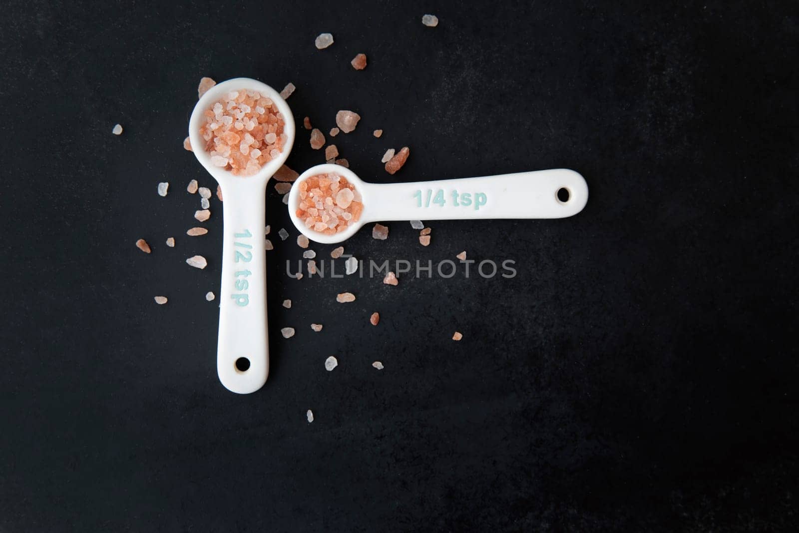 Pink Himalayan salt in measuring spoons on black background.