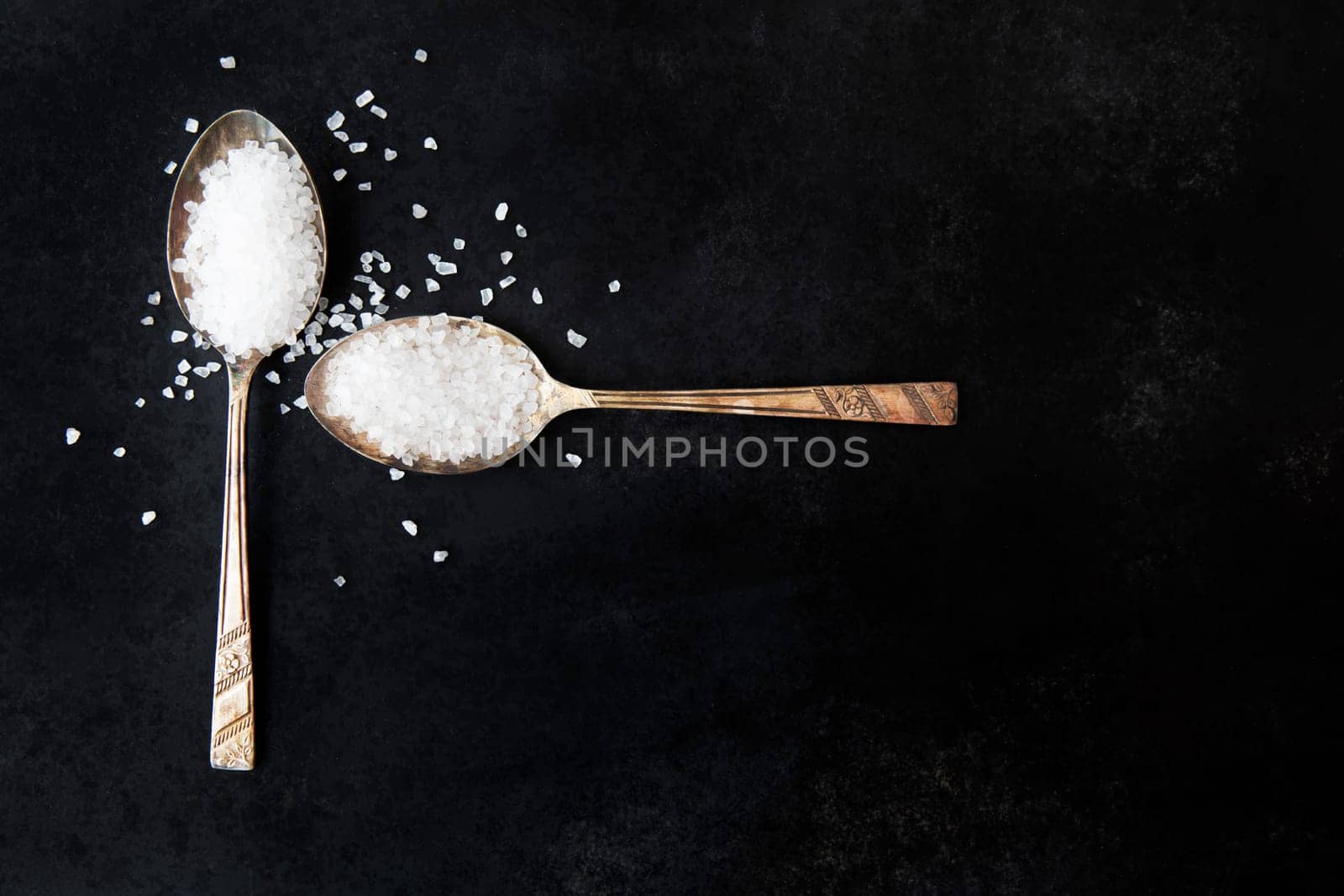 Salt crystals in old spoons on black background.