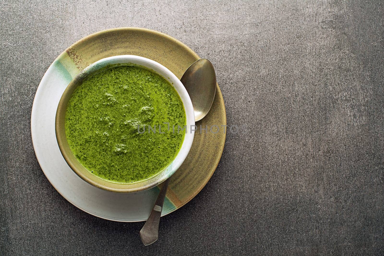 Spring healthy food. Green creamy soup with vegetables and herbs on gray background