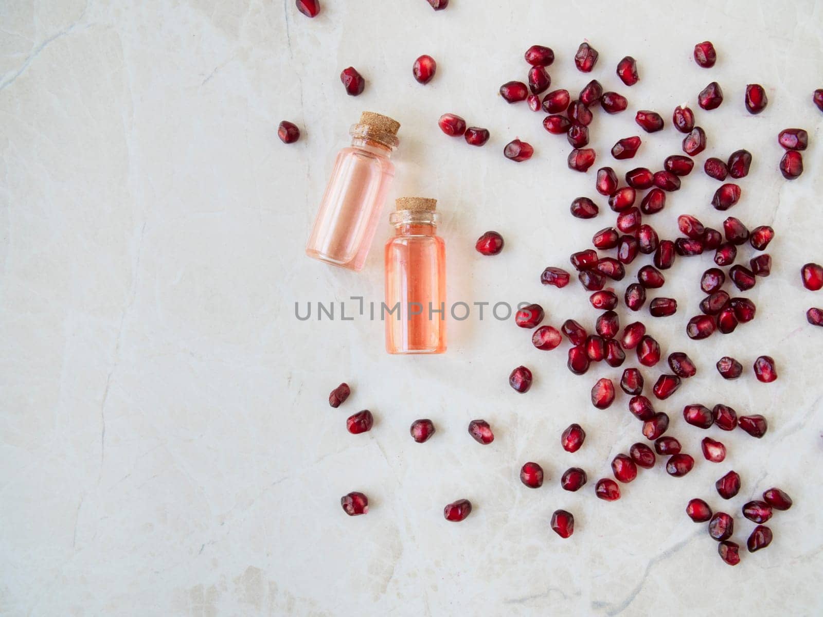 Flat lay pomegranate seeds with small bottles of extract on marble surface with copy space.