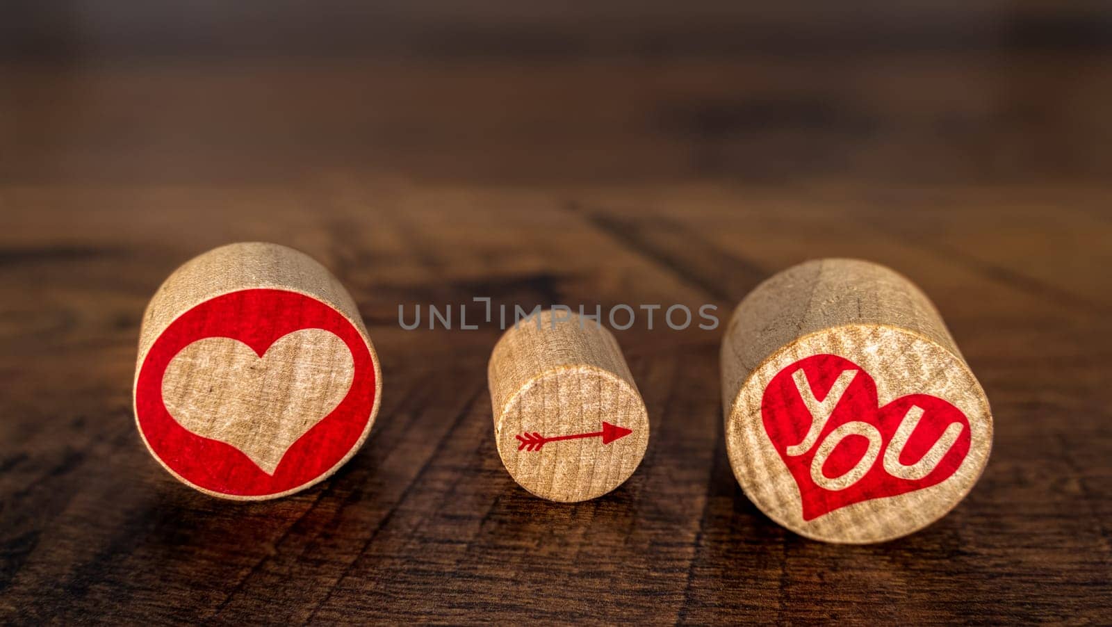 Love You illustrated with red hart pointing arrow on You in red hart on cork pieces Valentines Day idea on vintage oak, front view fading in distance