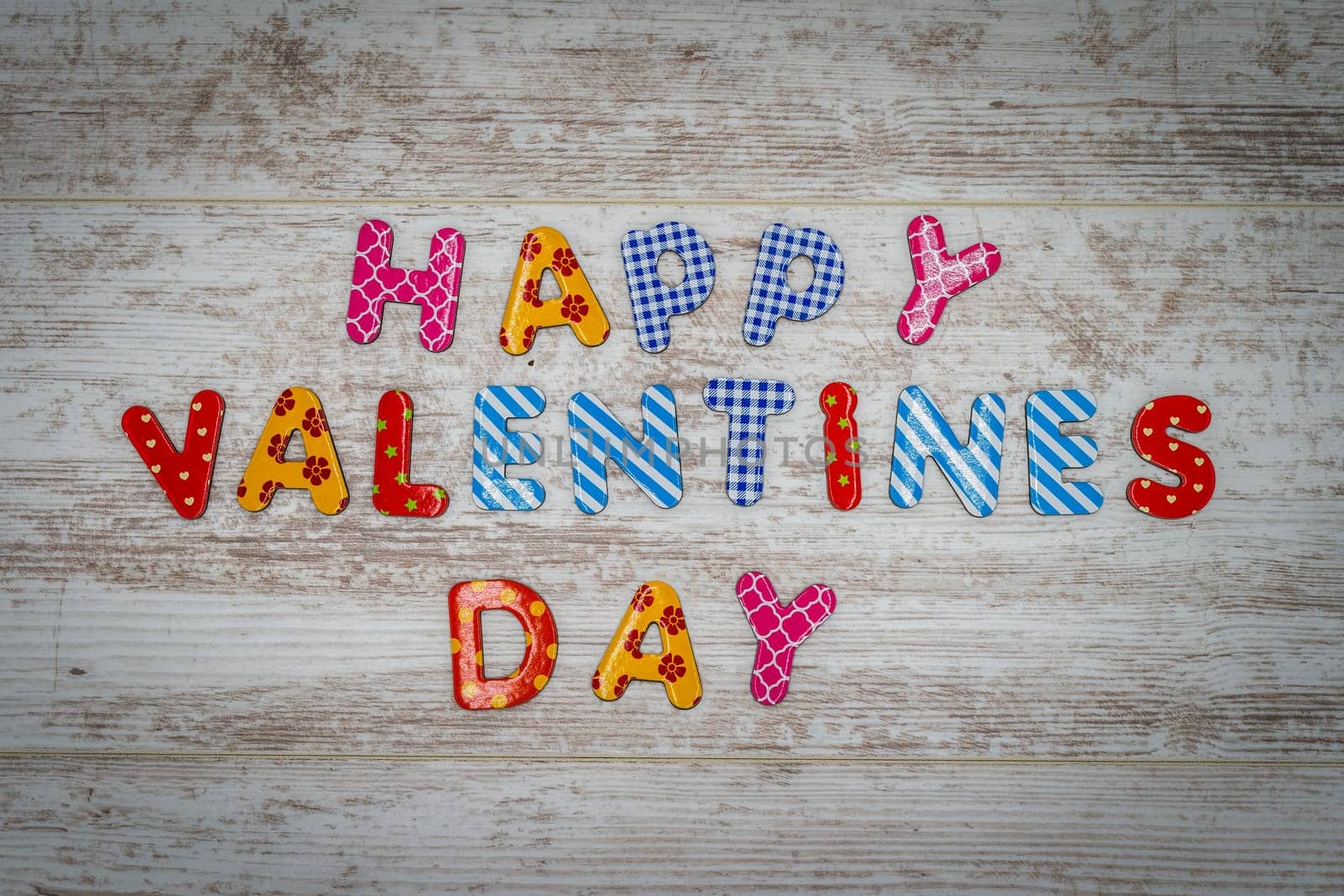 Happy Valentines Day made of single colourful letters in lines on white painted vintage oak panels
