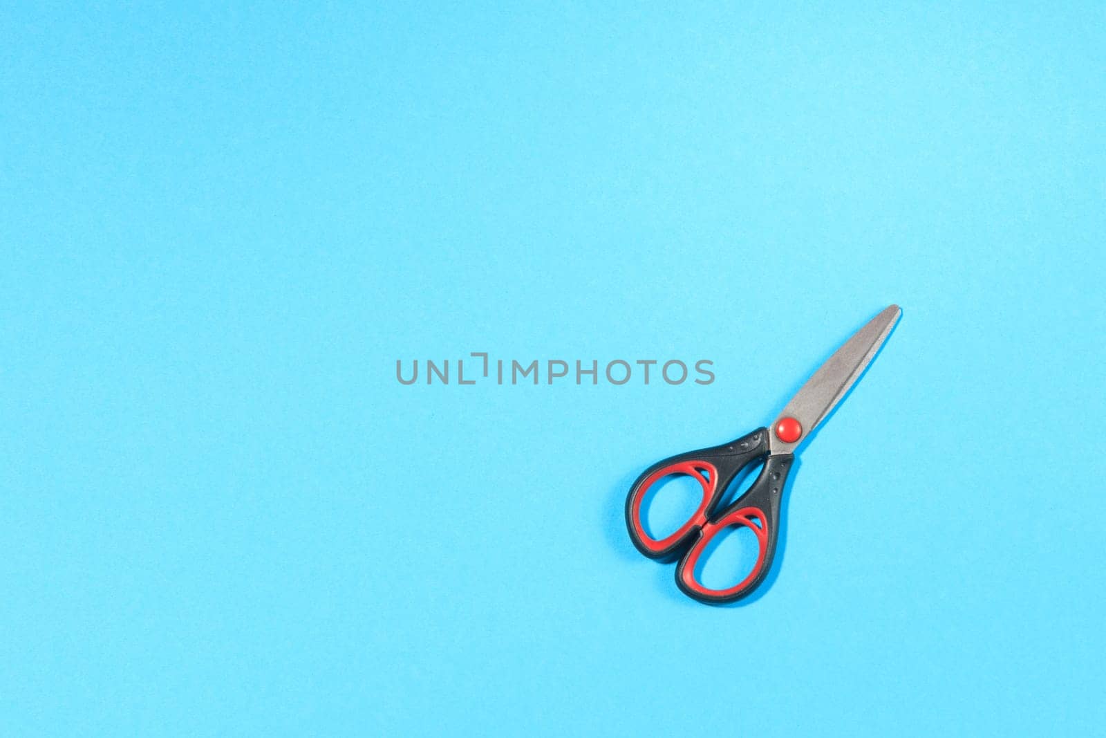 closed black scissors with red elements on blue background