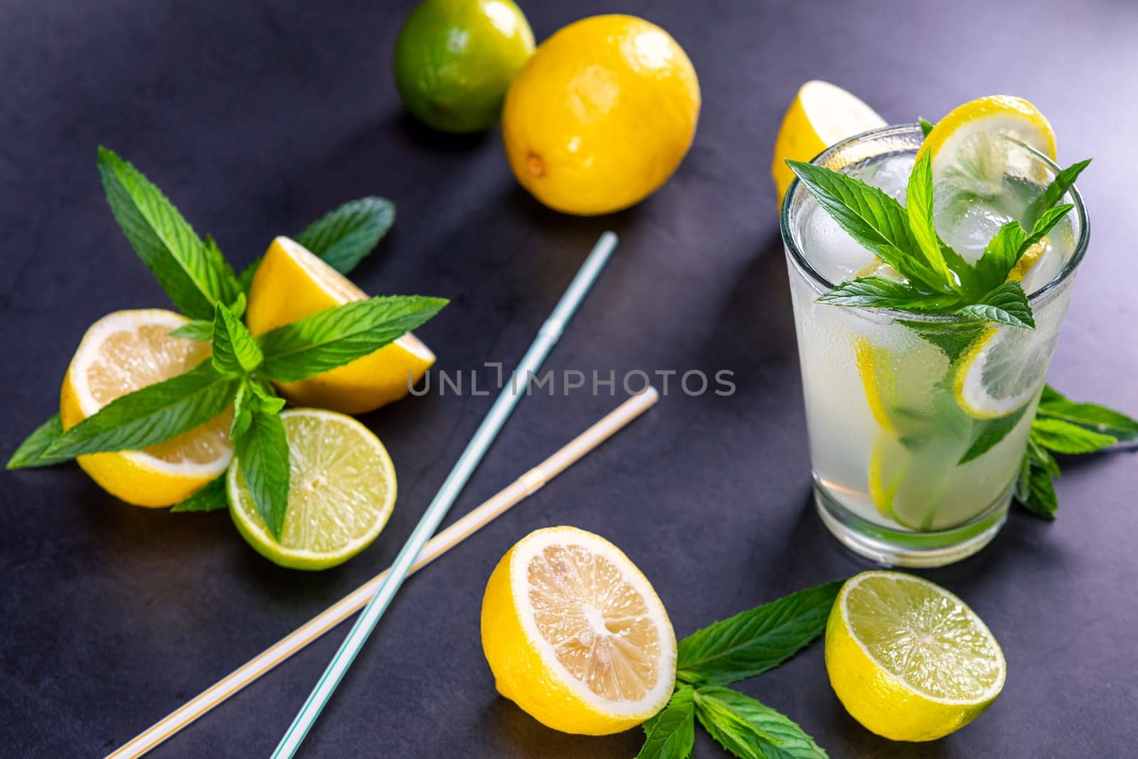 Cold refreshing summer lemonade with mint in a glass on a grey and black background. Focus on leaf in glass.