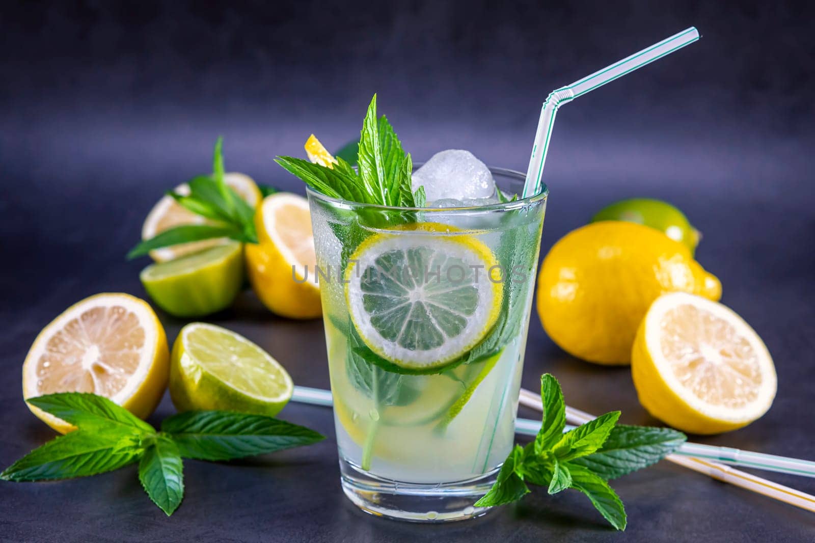Cold refreshing summer lemonade with mint in a glass on a grey and black background. Focus on leaf and ice in glass.