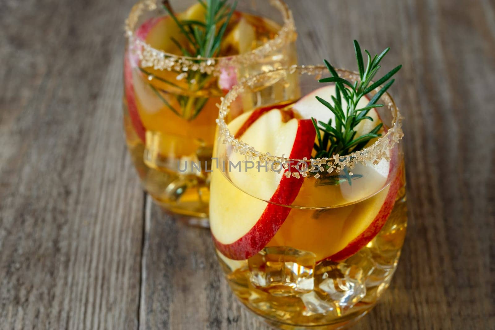 Apple drink with apple slices in a glass, a sprig of rosemary and brown sugar on the rim of a glass