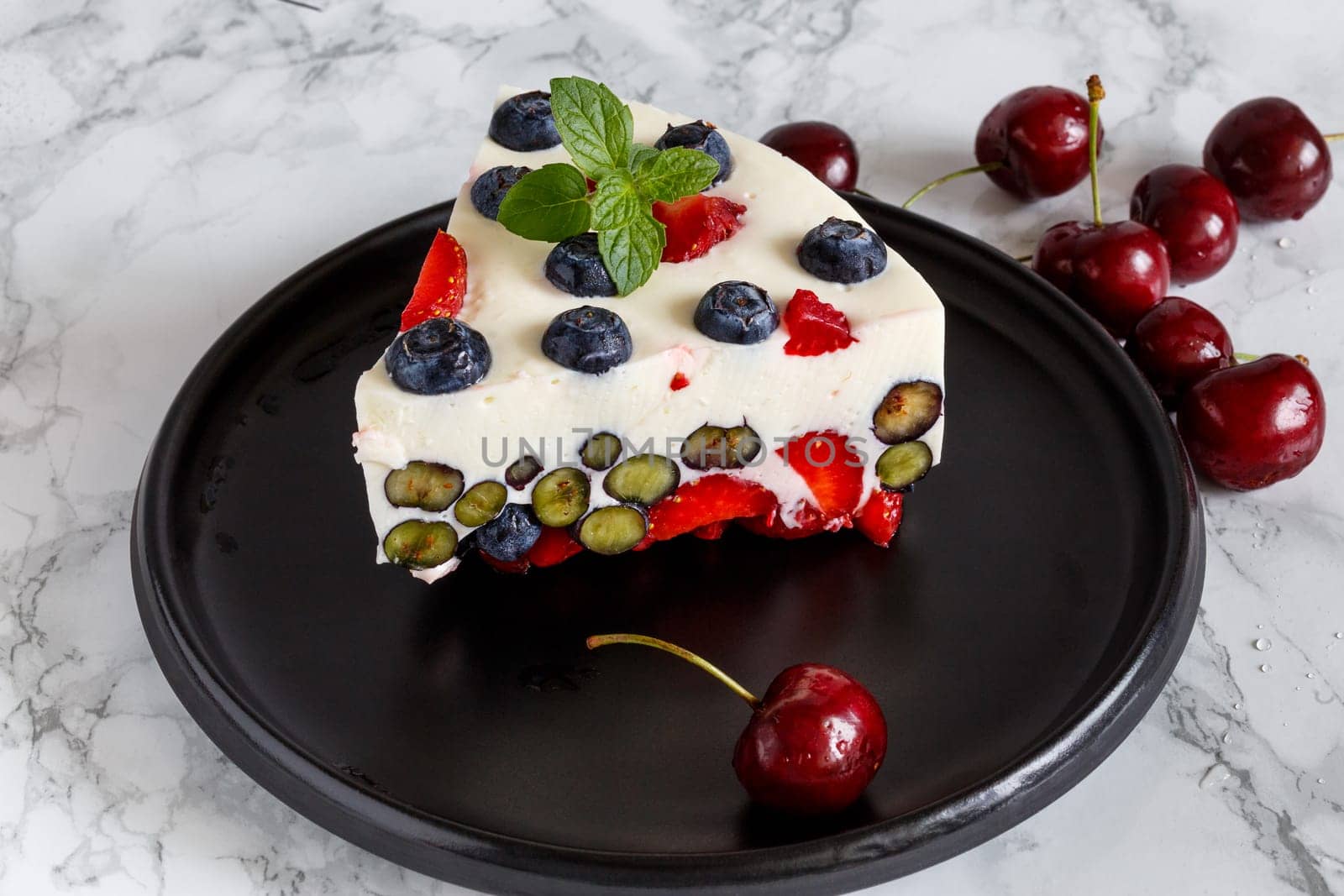 Berry dessert with blueberries and strawberries on the basis of yogurt on a black ceramic dish decorated with berries and mint