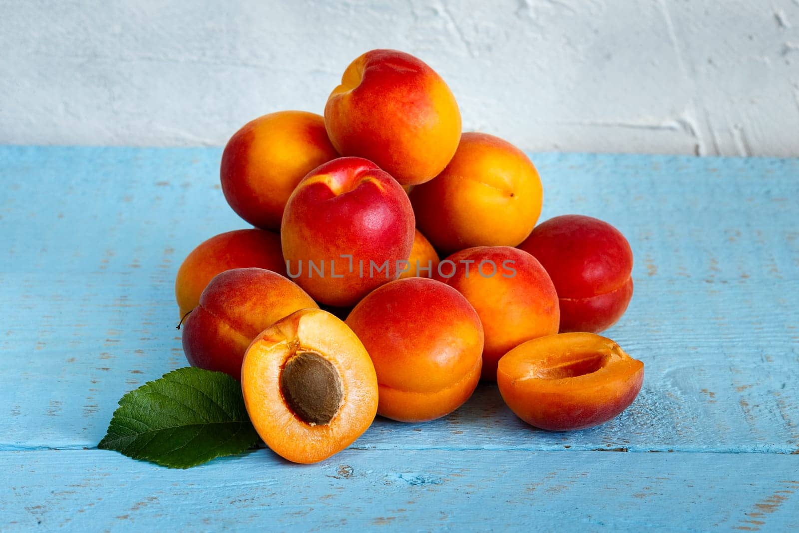 A bunch of ripe apricots on a wooden background, painted in blue, with a cut berry in front
