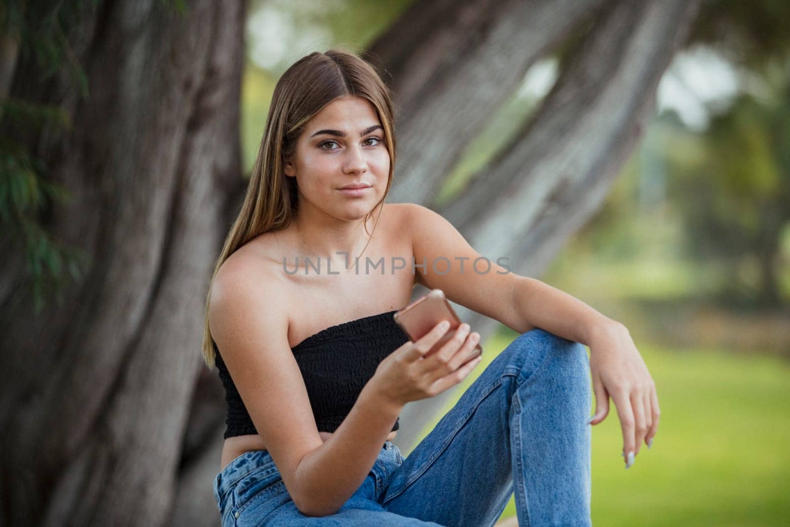 A teenage girl is relaxing on a park bench, using her mobile phone.