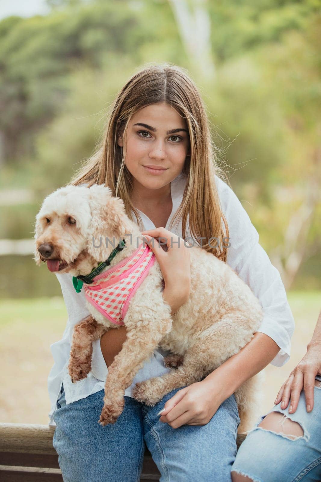 A teenage girl is sitting with her adorable puppy on her lap outdoors.
