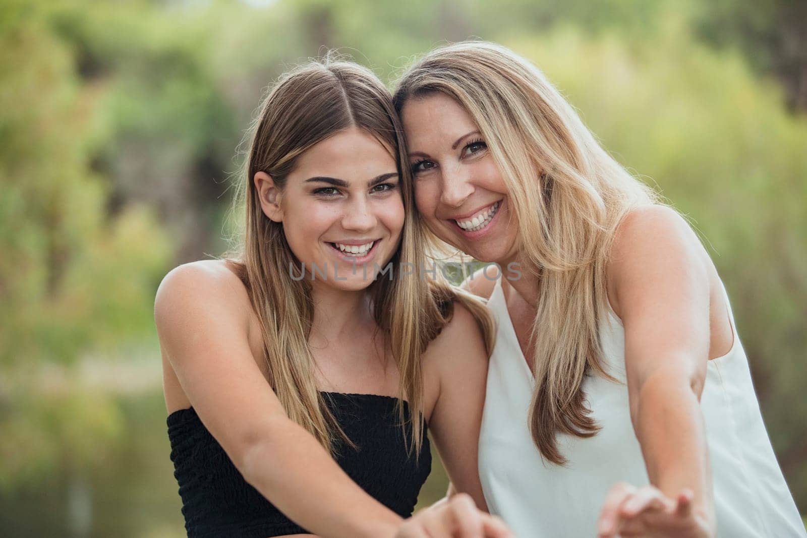 A beautiful mother and her daughter and standing side by side outdoors, laughing together and looking carefree.