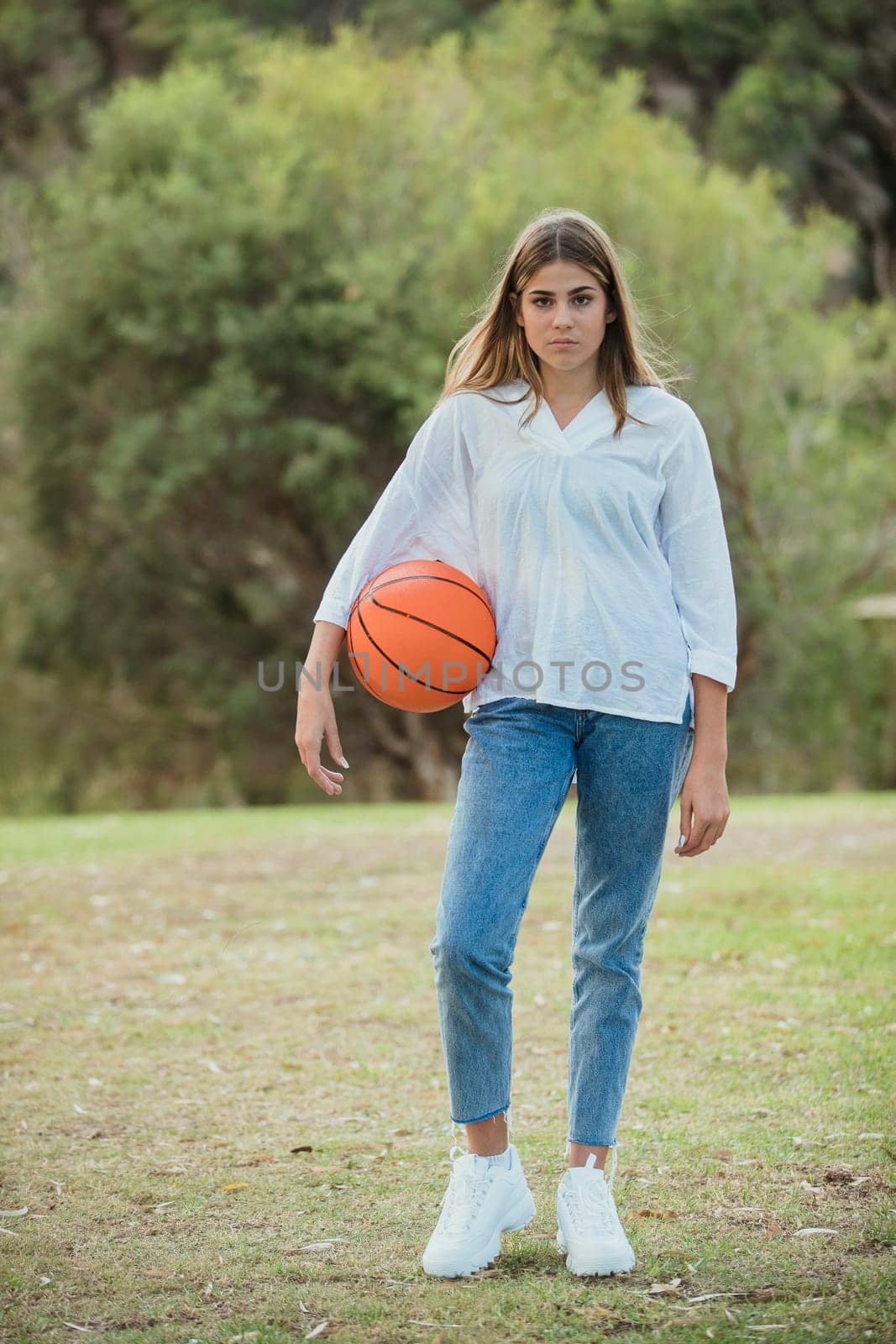 A teenage girl standing with a basketball outdoors.