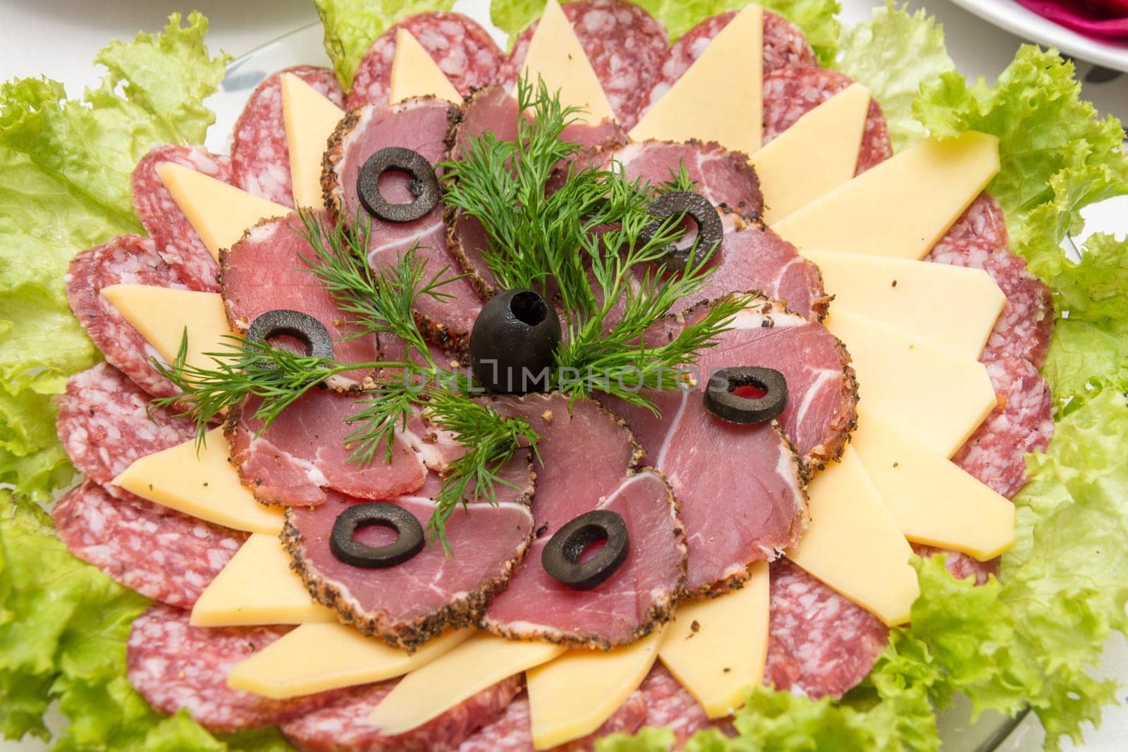 Sliced on a plate of sausage and cheese, decorated with greens and olives