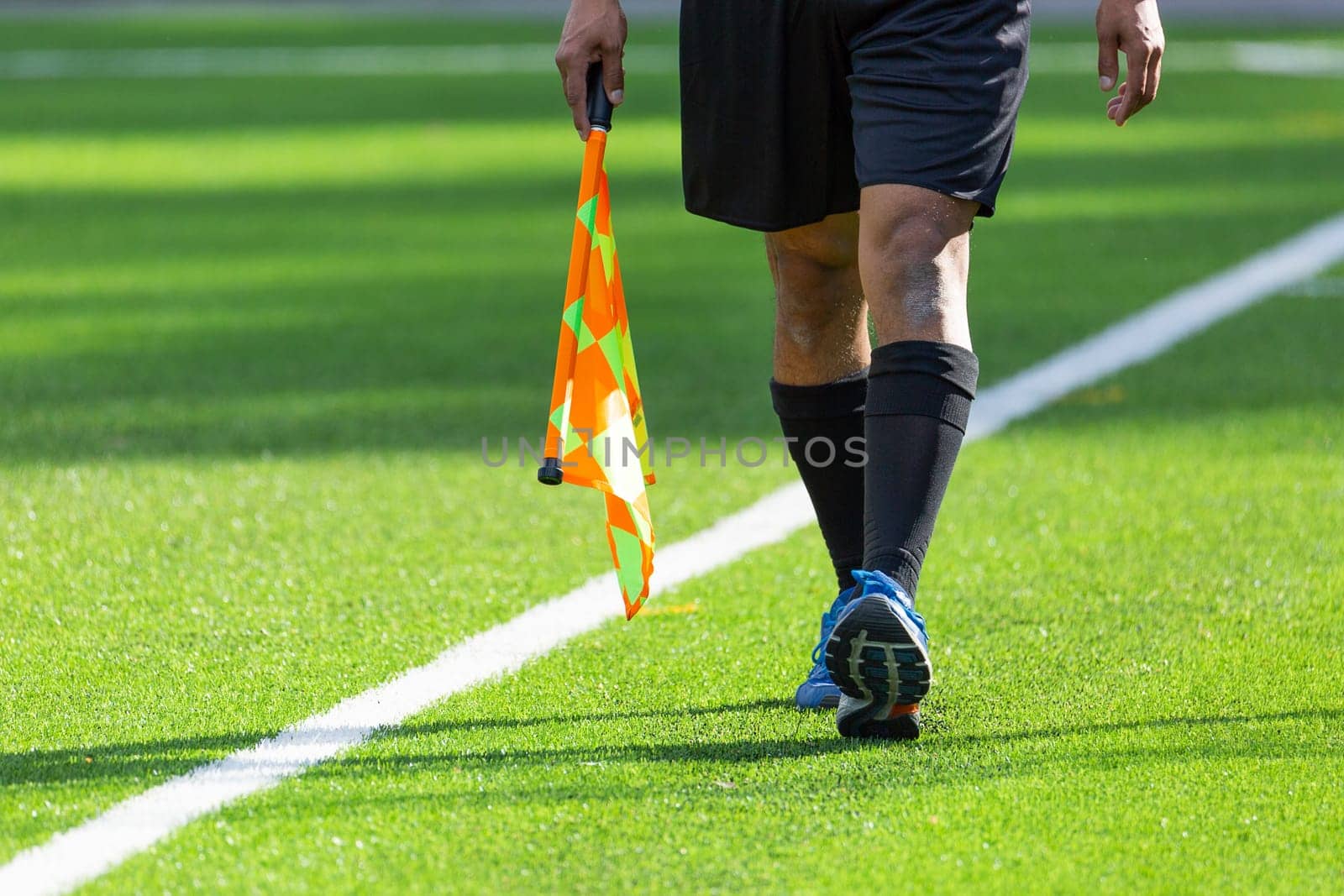 Football Assistant Referee walking with Flag on artificial turf.