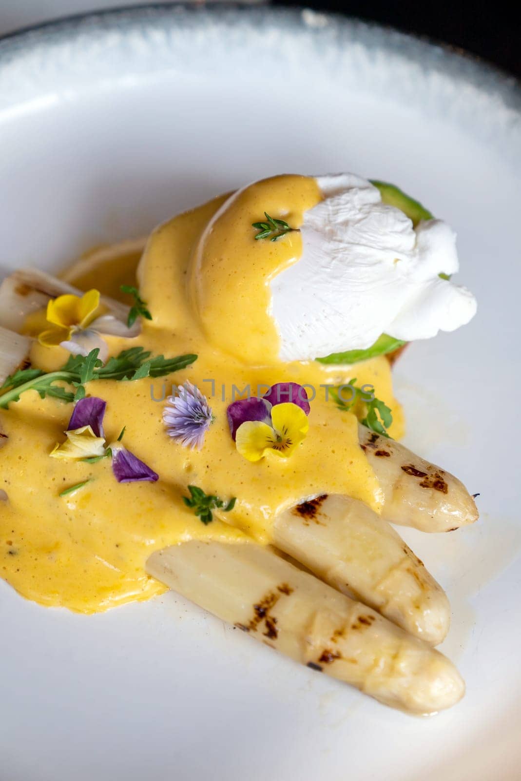 Gourmet grilled white asparagus with poached egg serve with hollandaise savory sauce decorate with edible colorful flowers