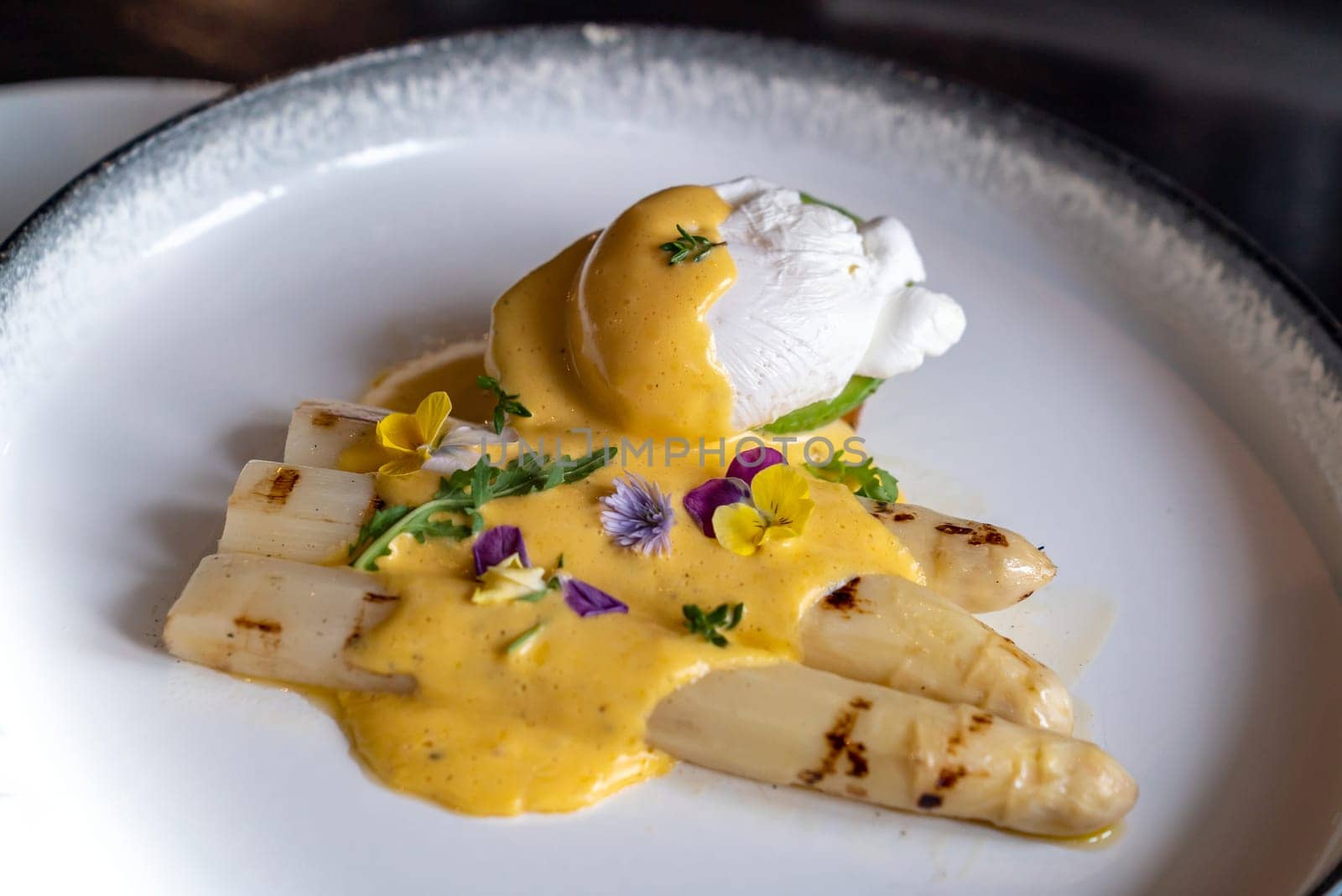 Gourmet grilled white asparagus with poached egg serve with hollandaise savory sauce decorate with edible colorful flowers