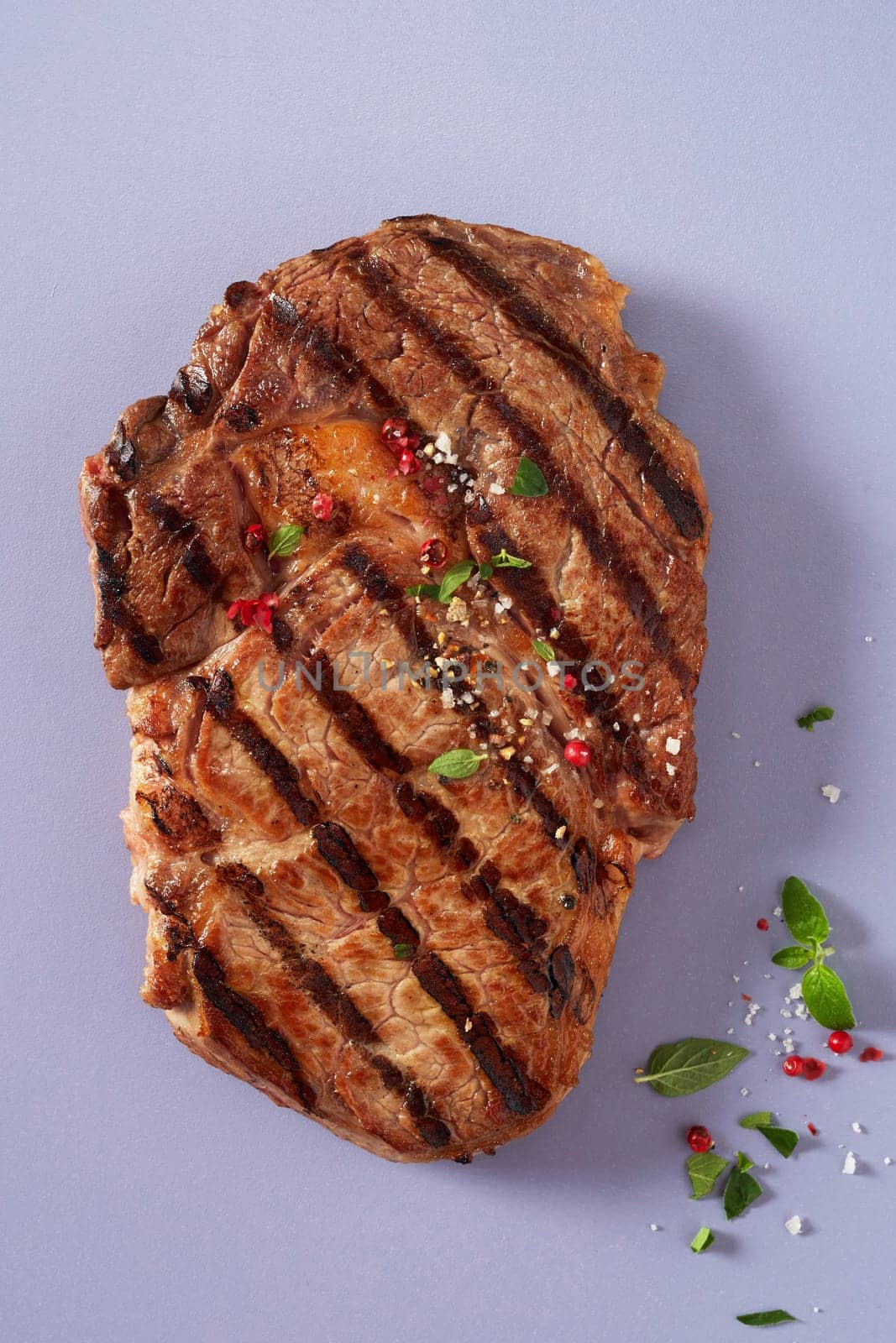 Portion of lean tender marinated grilled beef steak seasoned with fresh herbs, spices and salt on a blue grey background viewed from above