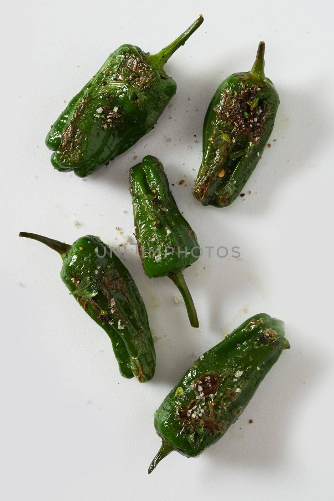 Grilled or roasted spicy seasoned whole green Jalopeno chili peppers scattered on white viewed from above