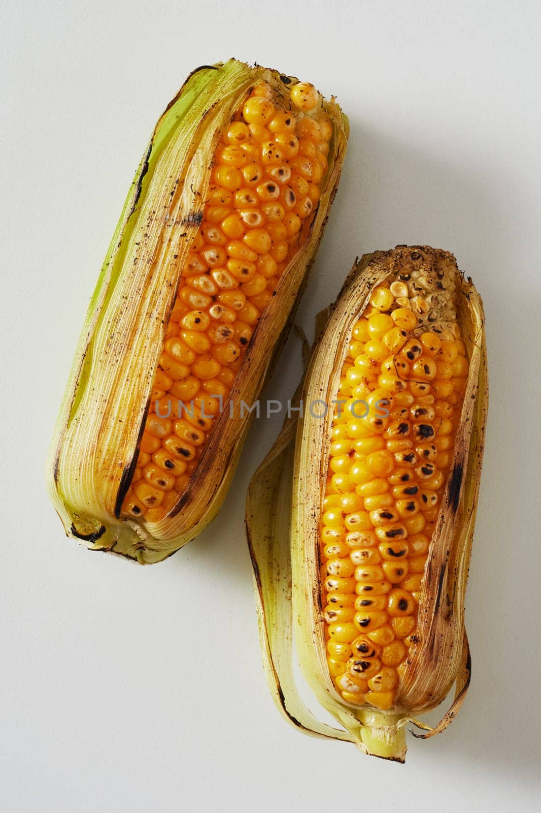 Two delicious barbecued corncobs, maize or mealies with their outer leaves fresh from a summer barbecue