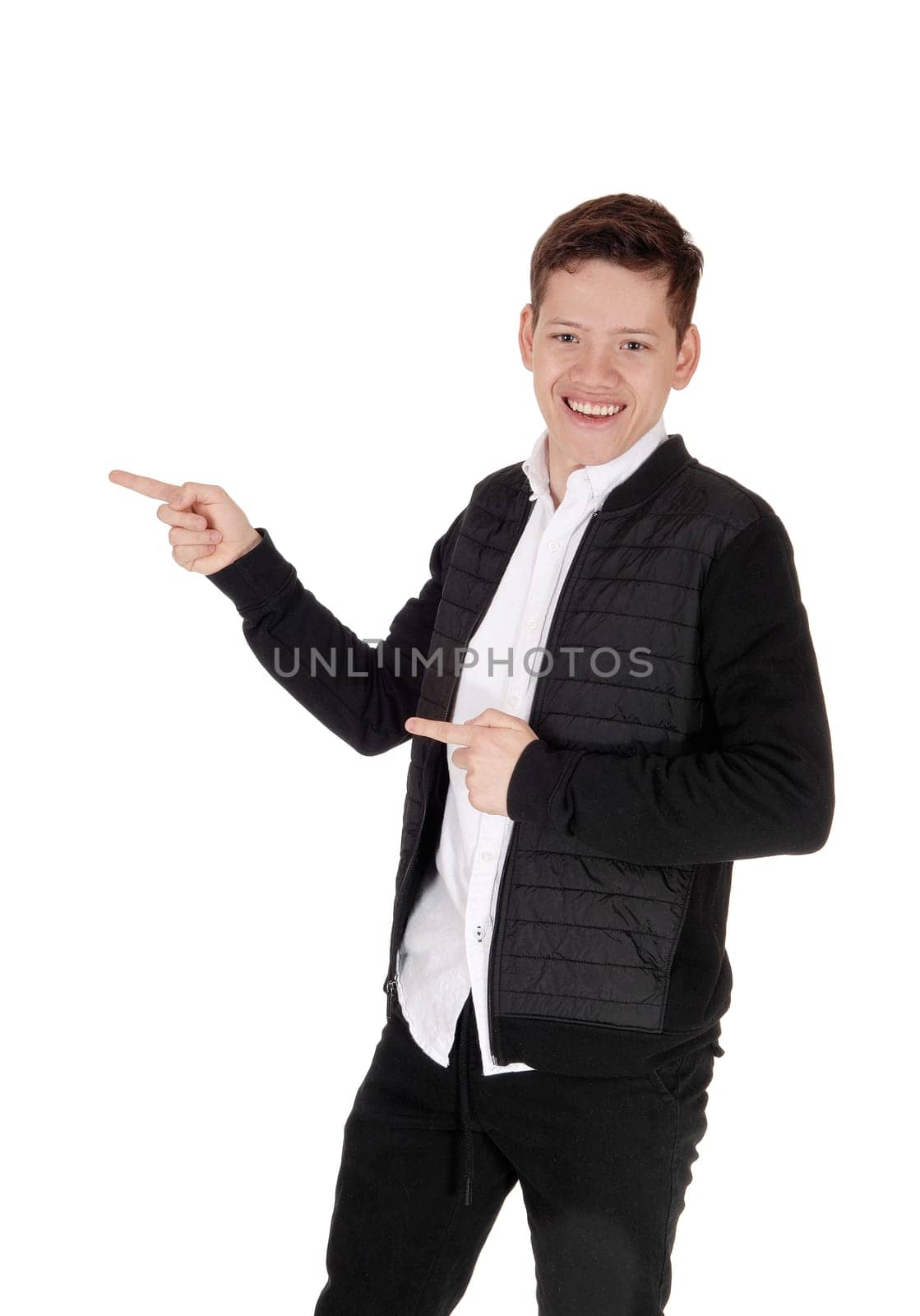 A handsome young teenager boy standing in a black jacket and white .shirt, pointing with both hands away, isolated for white background.