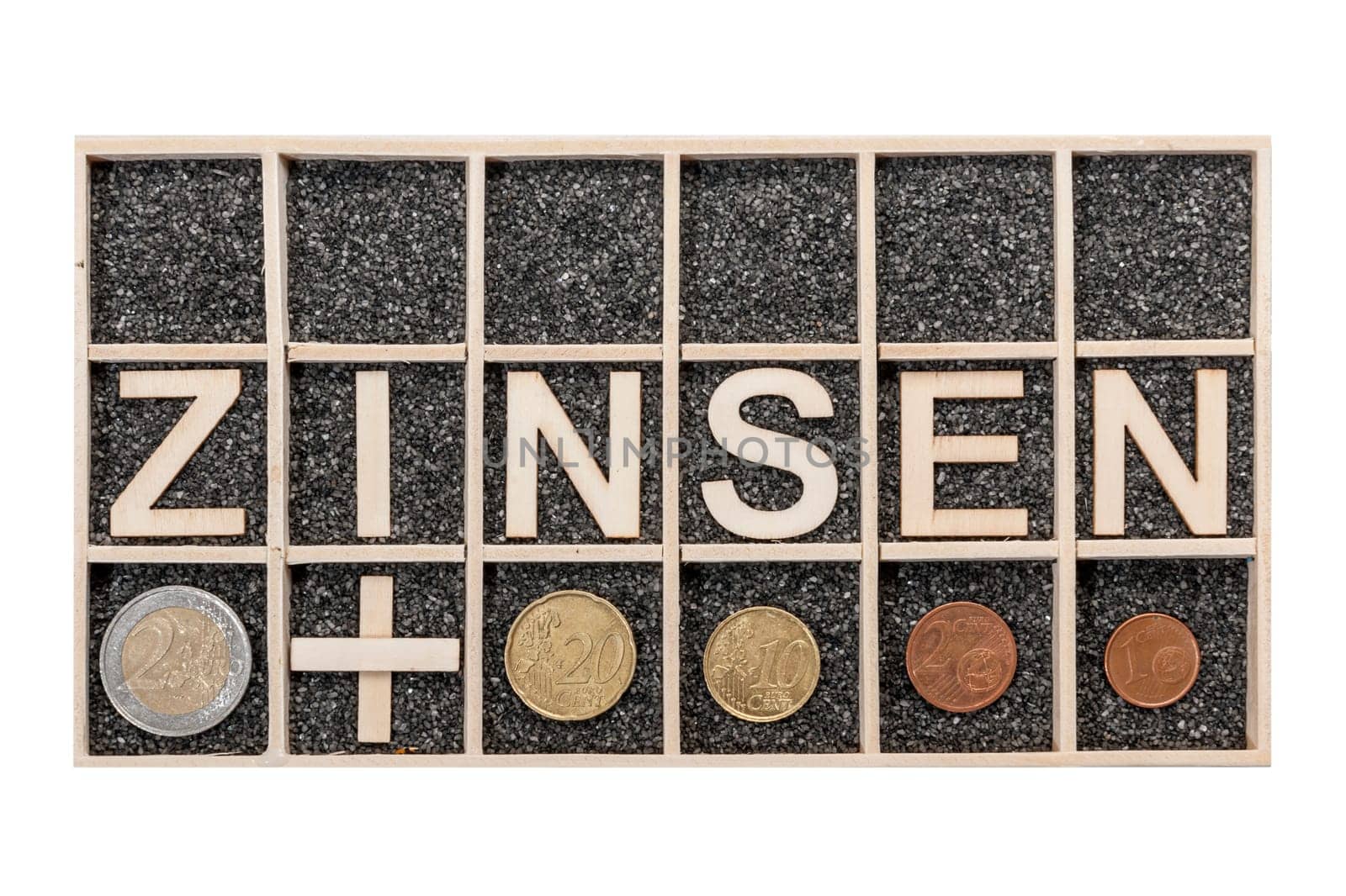 Plywood letters arranged in a collecting box with black decorative sand depicting the word ZINSEN and some Euro coins a nearby subjects in top view isolated on white.
