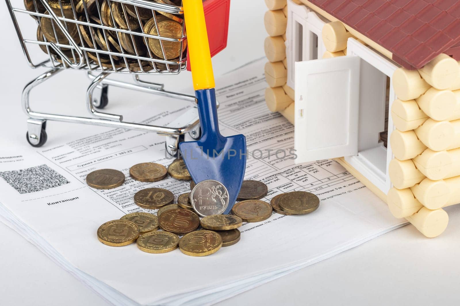 A shovel with a ruble coin rests on a money cart, a number of apartment bills and a toy house