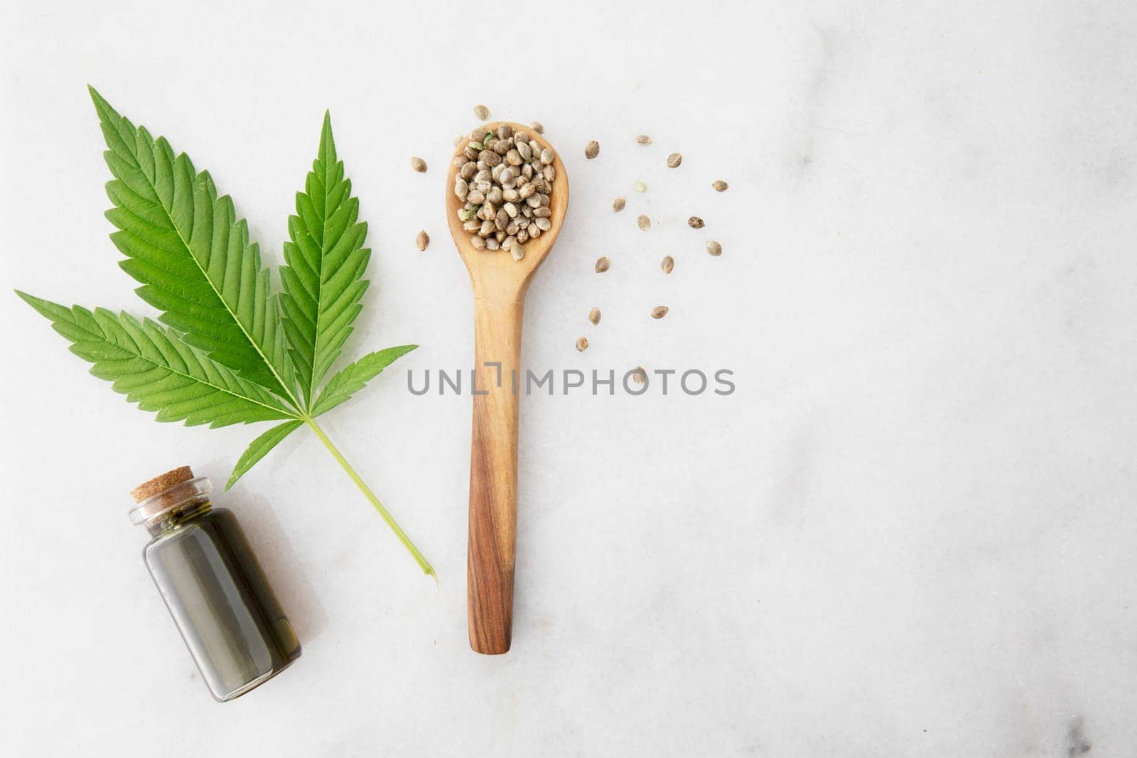 Small bottle of CBD oil with cannabis leaf and seeds in a wooden spoon, viewed from directly above.