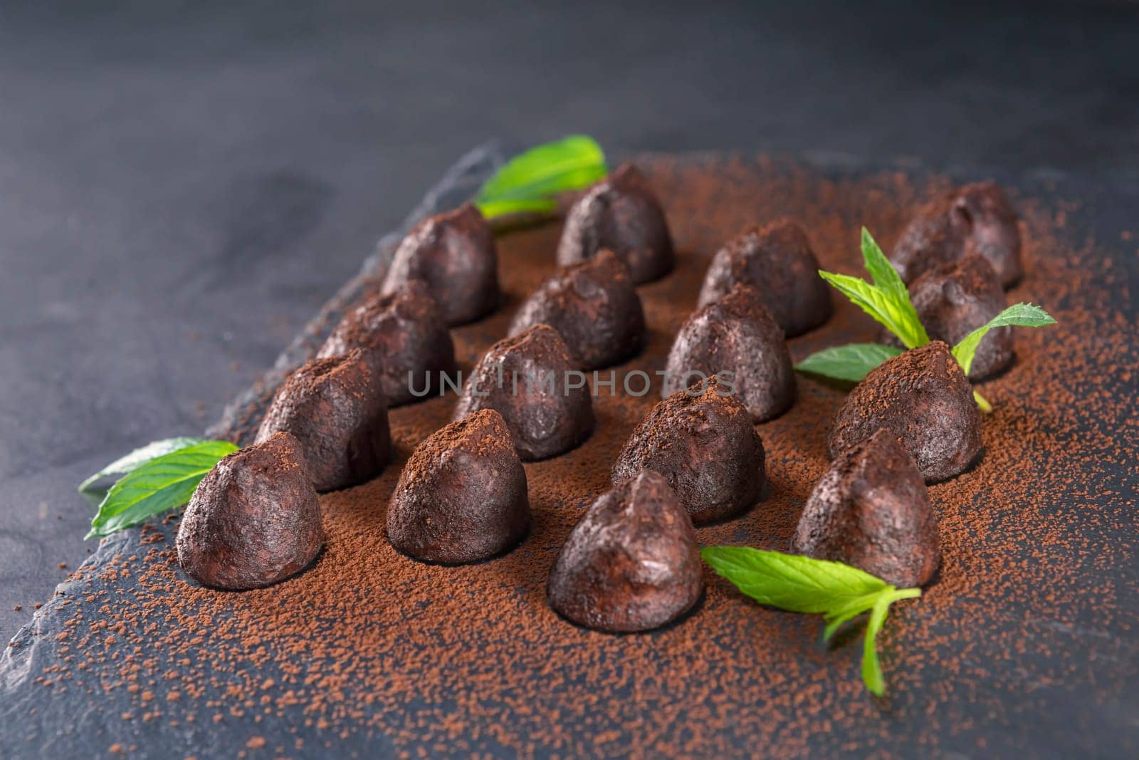 Homemade chocolate truffles with mint sprinkled with cocoa powder on slate. Focus on second truffle in road.