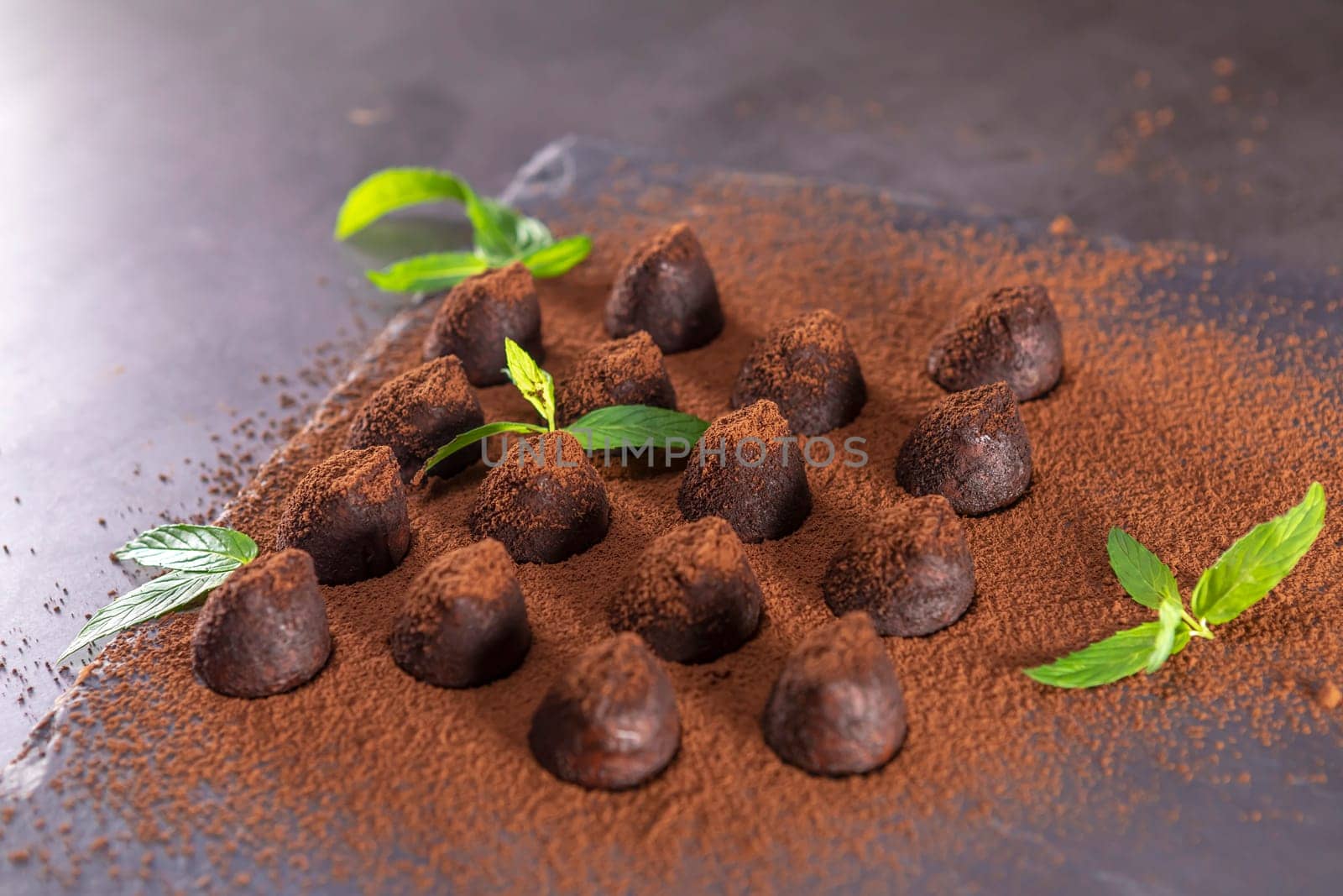Homemade chocolate truffles with mint sprinkled with cocoa powder on slate. Focus on truffle.