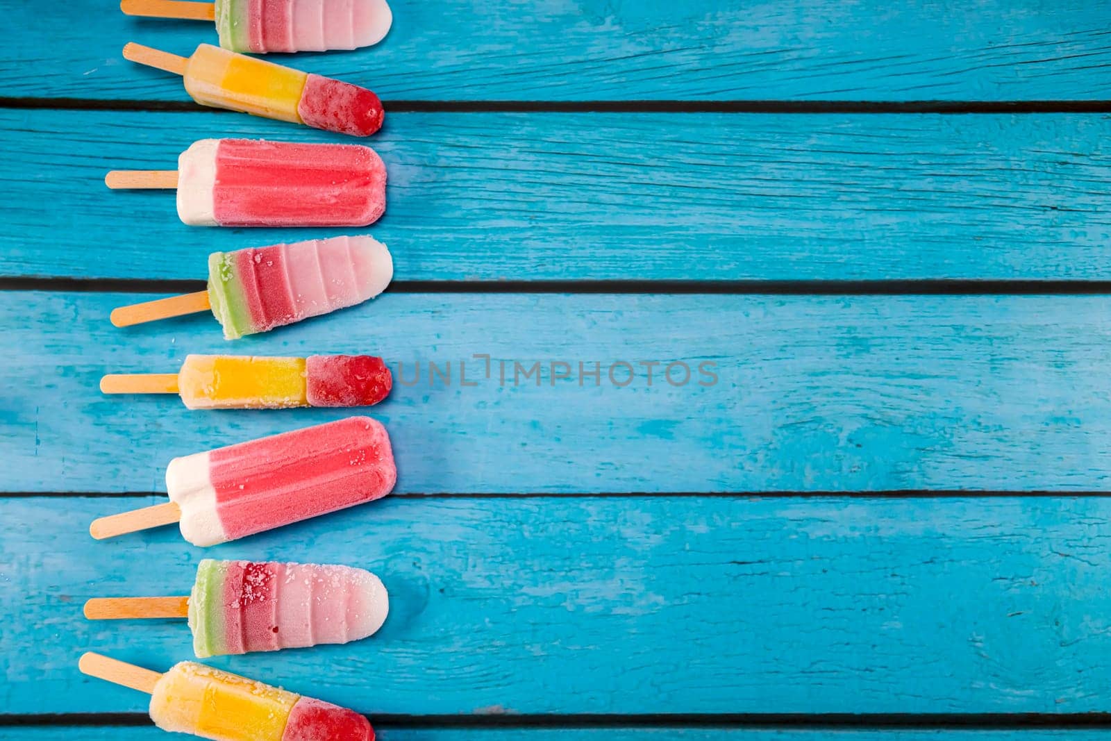 Colorful fruit ice cream stick look fresh to eat placed on a blue vintage wooden. Focus on ice crean sticks.