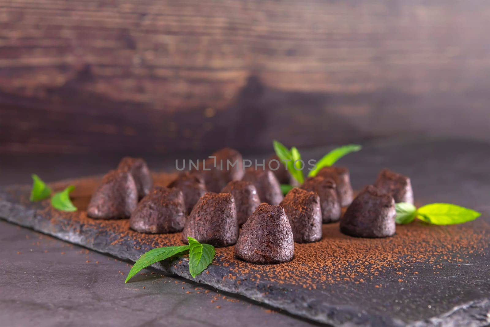 Homemade chocolate truffles with mint sprinkled with cocoa powder on slate. Focus on first truffle.