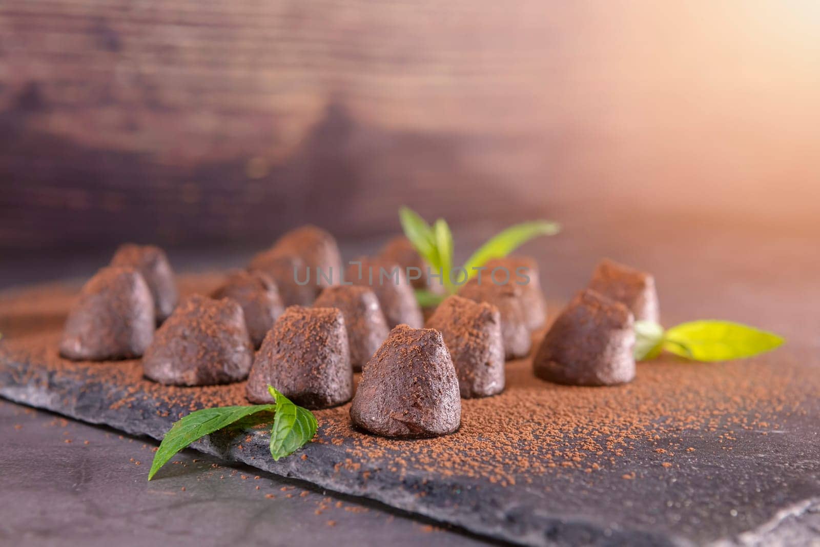 Homemade chocolate truffles with mint sprinkled with cocoa powder on slate. Focus on first truffle