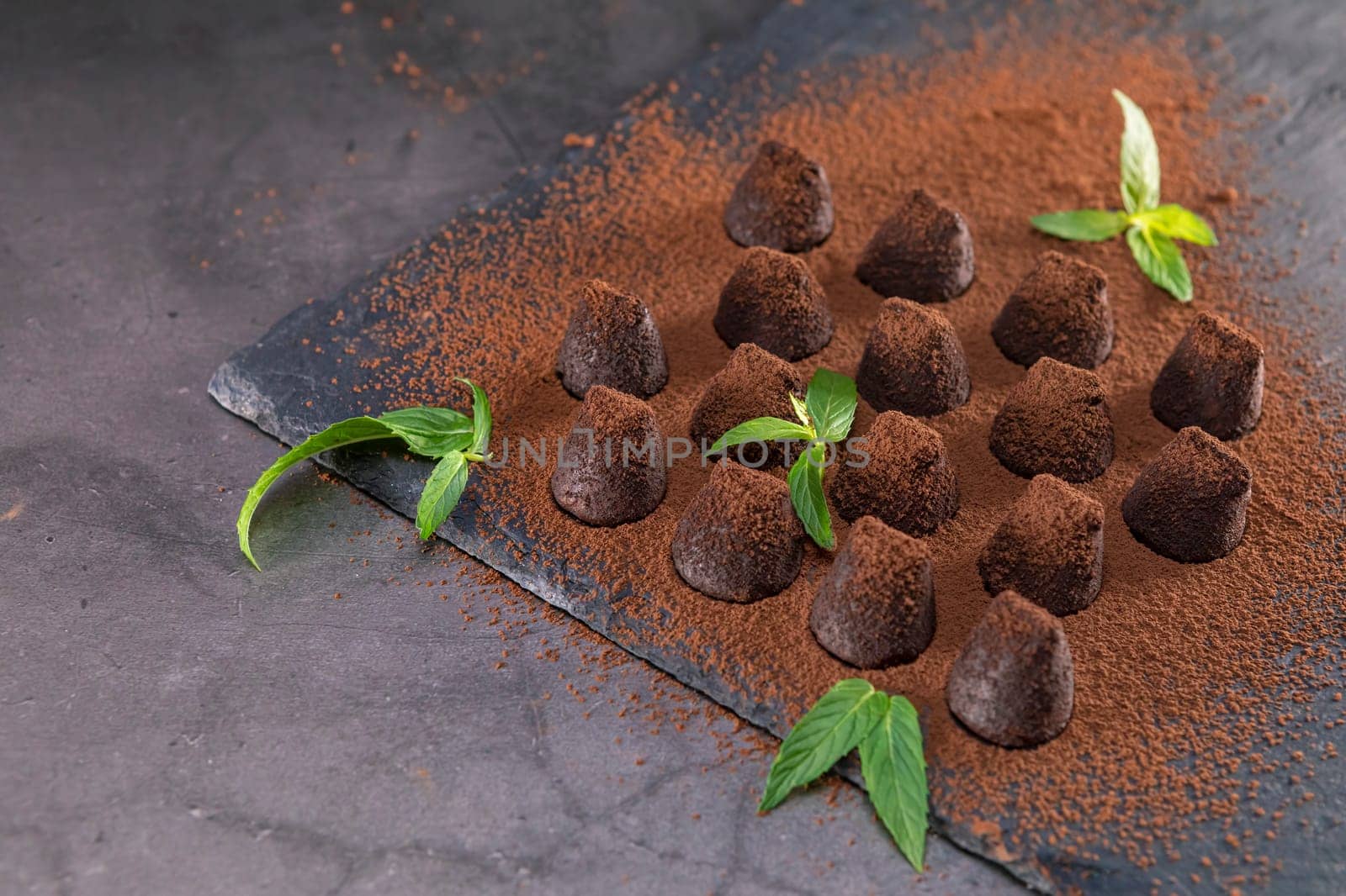 Homemade chocolate truffles with mint sprinkled with cocoa powder on slate. Focus on leaf.