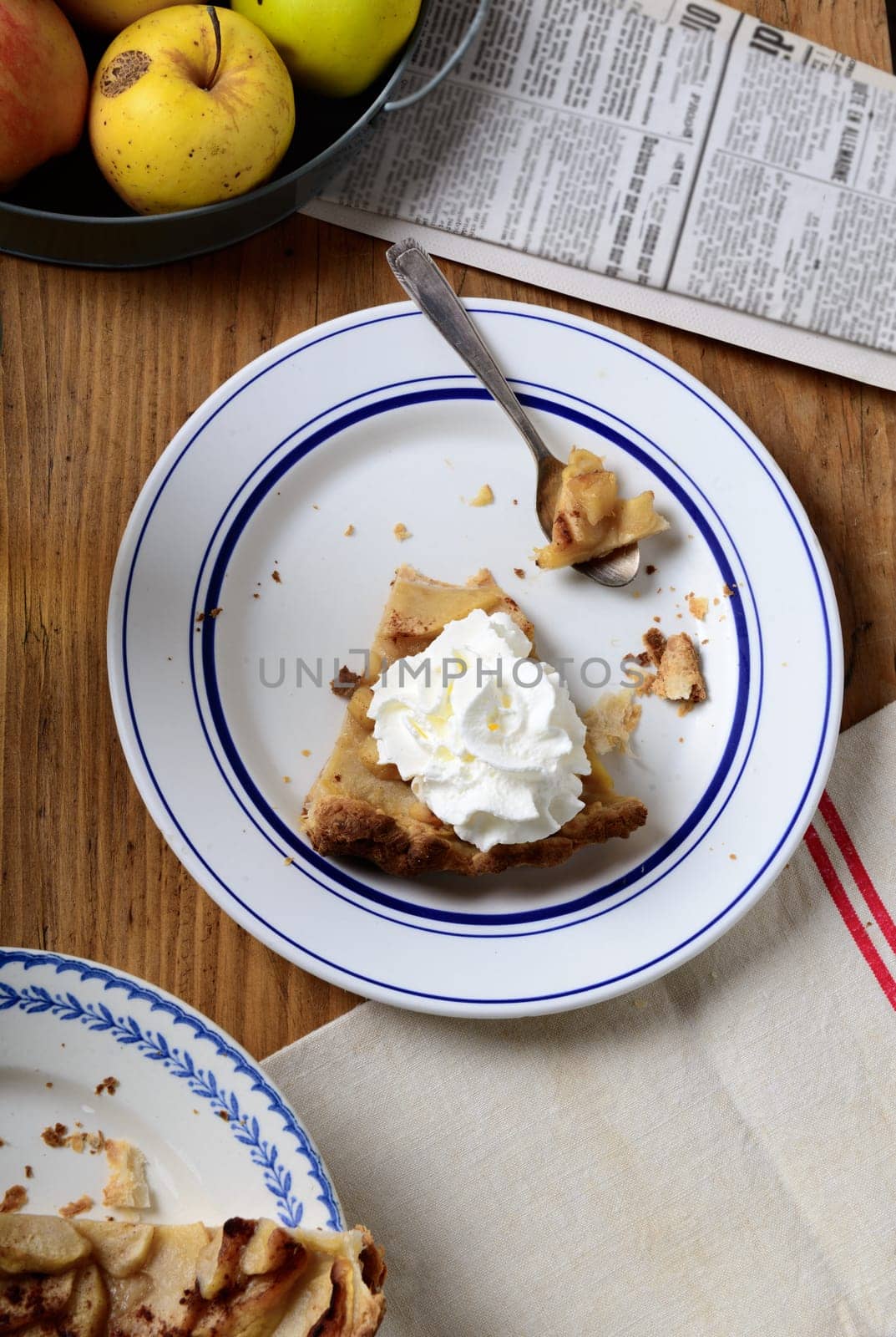 apple pie on a table with apples and whipped cream