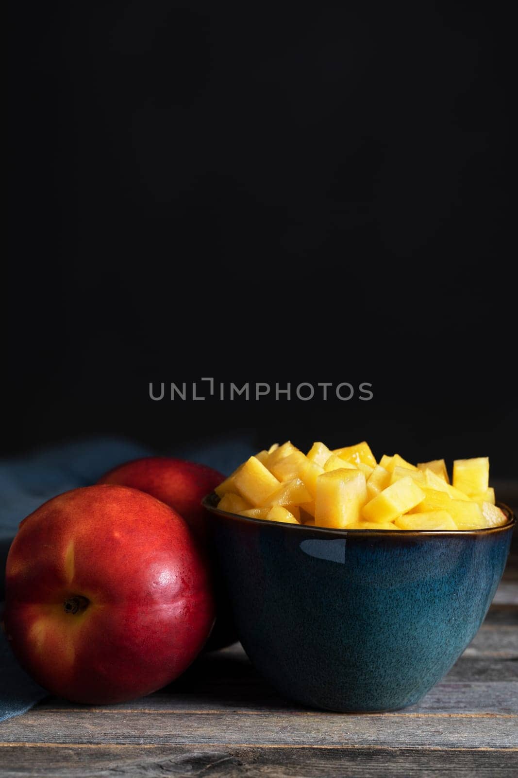 Chopped nectarines in bowl with whole nectarine on ths side, low key lighitng and vertical orientation.