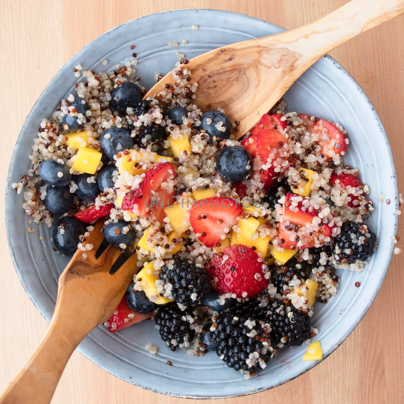 Blue bowl filled with fruit salad with quinoa,  strawberry slices, chopped nectarines. blackberries and blueberries on wooden surface, image 7 of 8