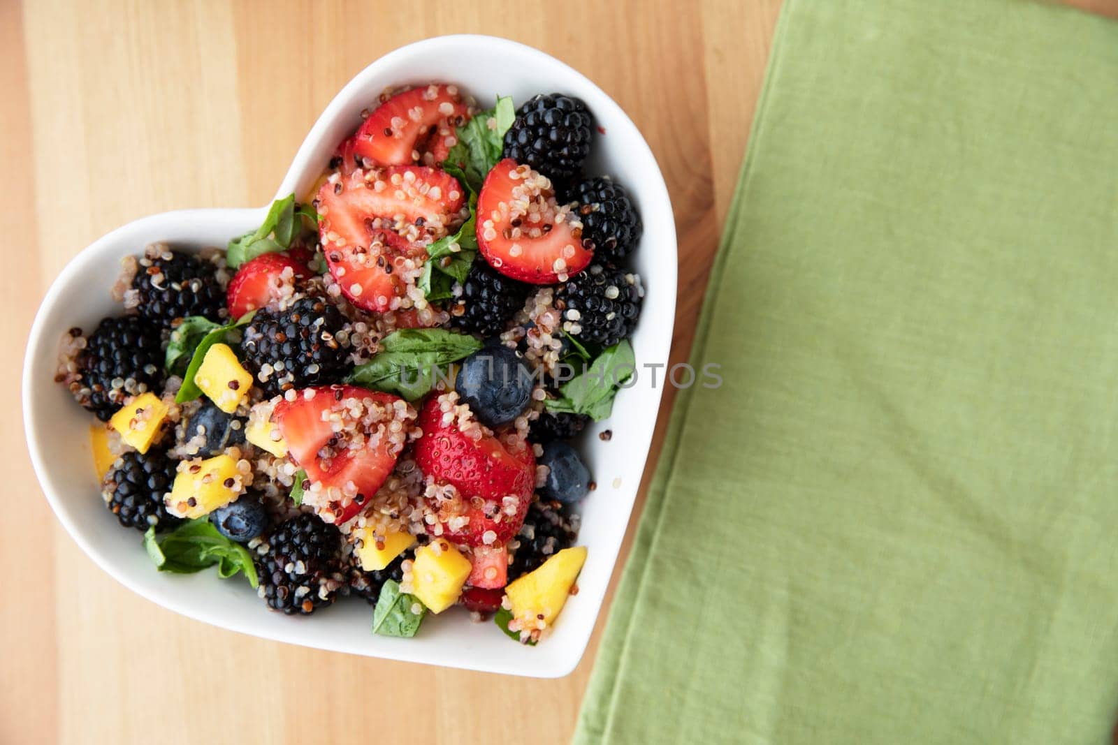 Healthy quinoa fruit salad in heart shaped bowl, flat lay with copy space