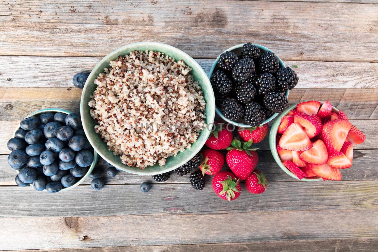 Flat lay of fres strawberries, blueberries, blackberreis and quinoain bowls.