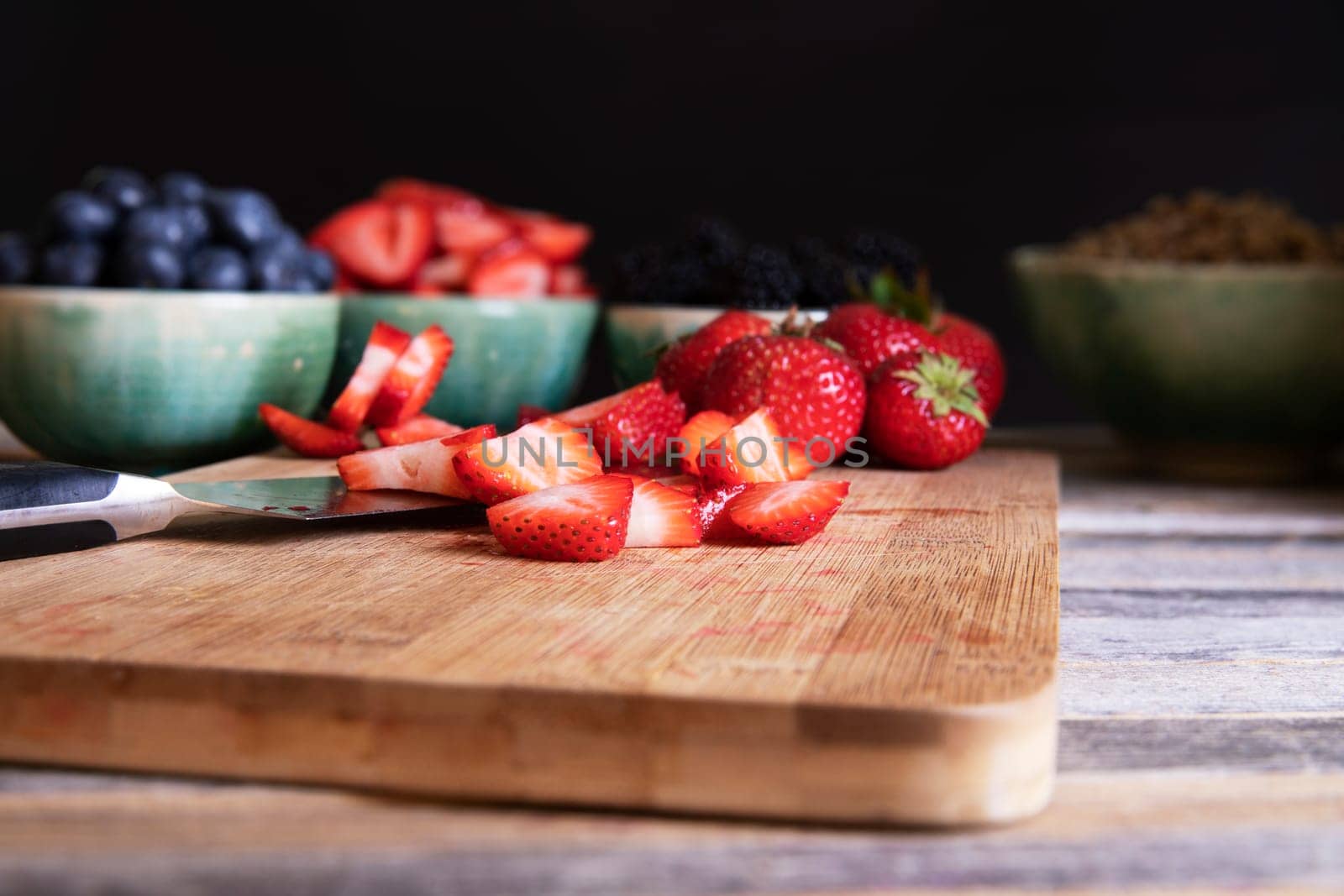Sliced and whole strawberries on cutting board with knife, low key lighitng and horizontal orientation.