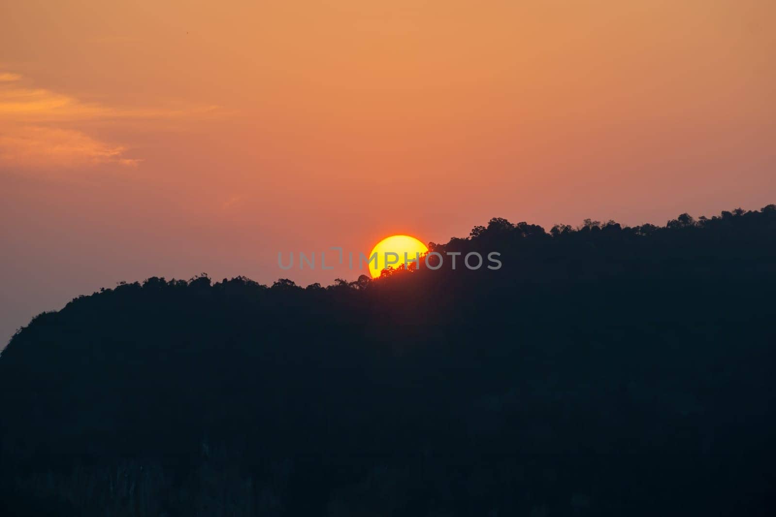 Sunrise behind the mountains, the shadows of the mountains, the orange sky with faint clouds.