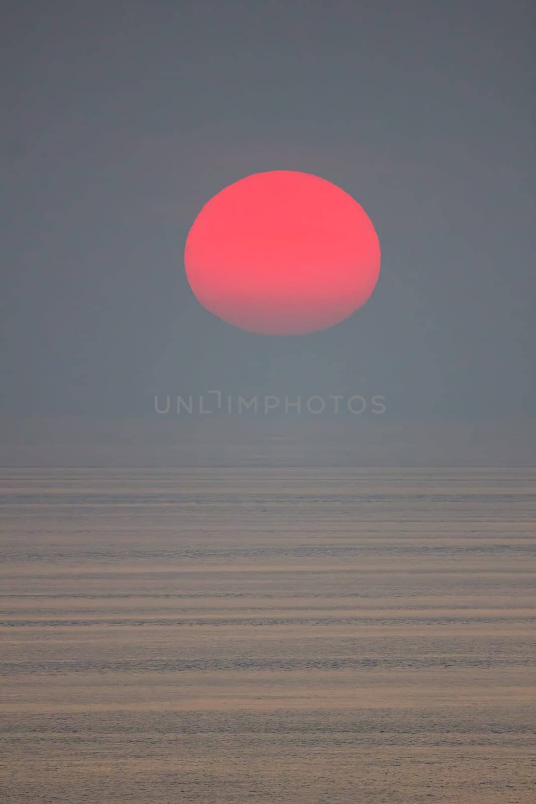 The sun is falling into the sea and being partially swallowed by the fog.  sky  is dark