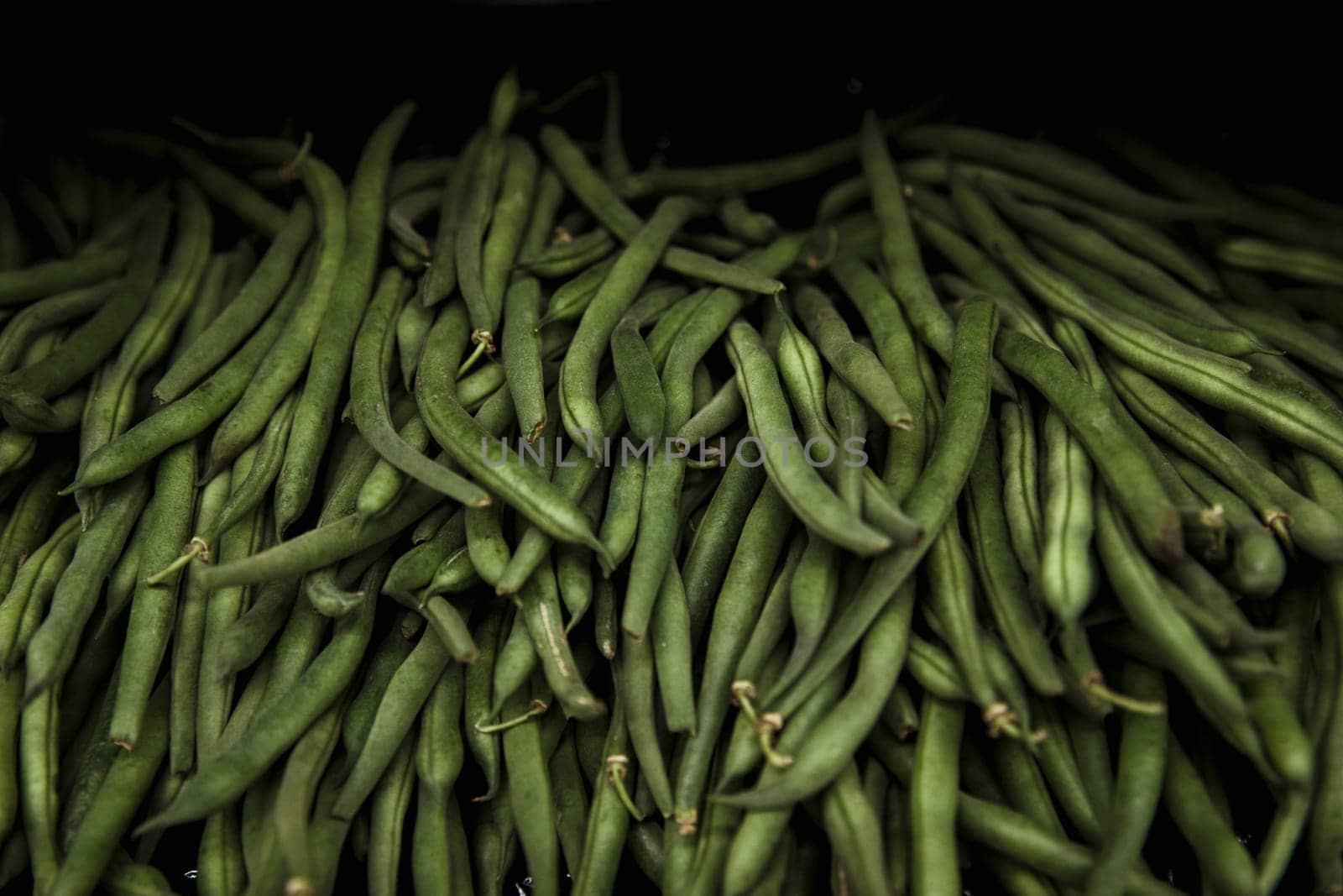 A close-up shot of an abundance of fresh green pea pods on display at a market stall.
