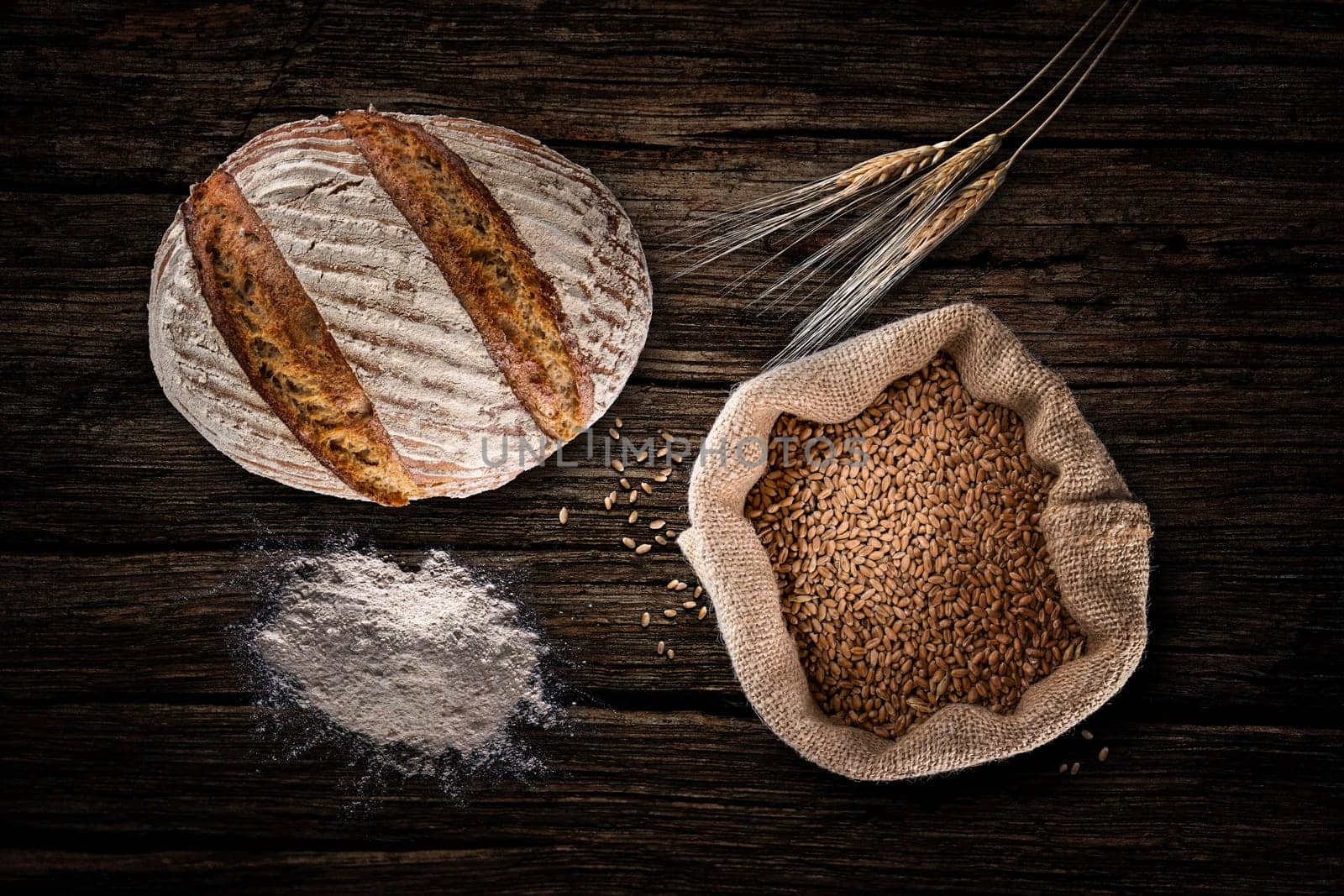 Still life with baking rye bread, ears, flour and bag of grains in a sackcloth on old wood background