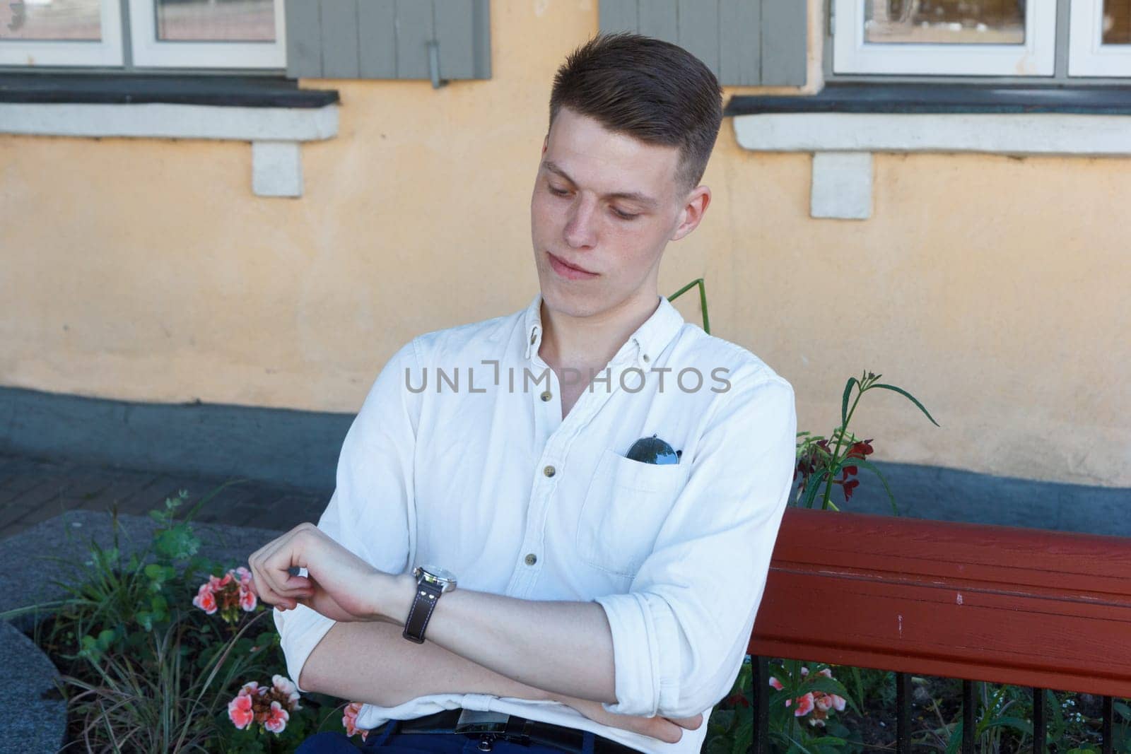 Young man relaxing on park bench and looking at his watch