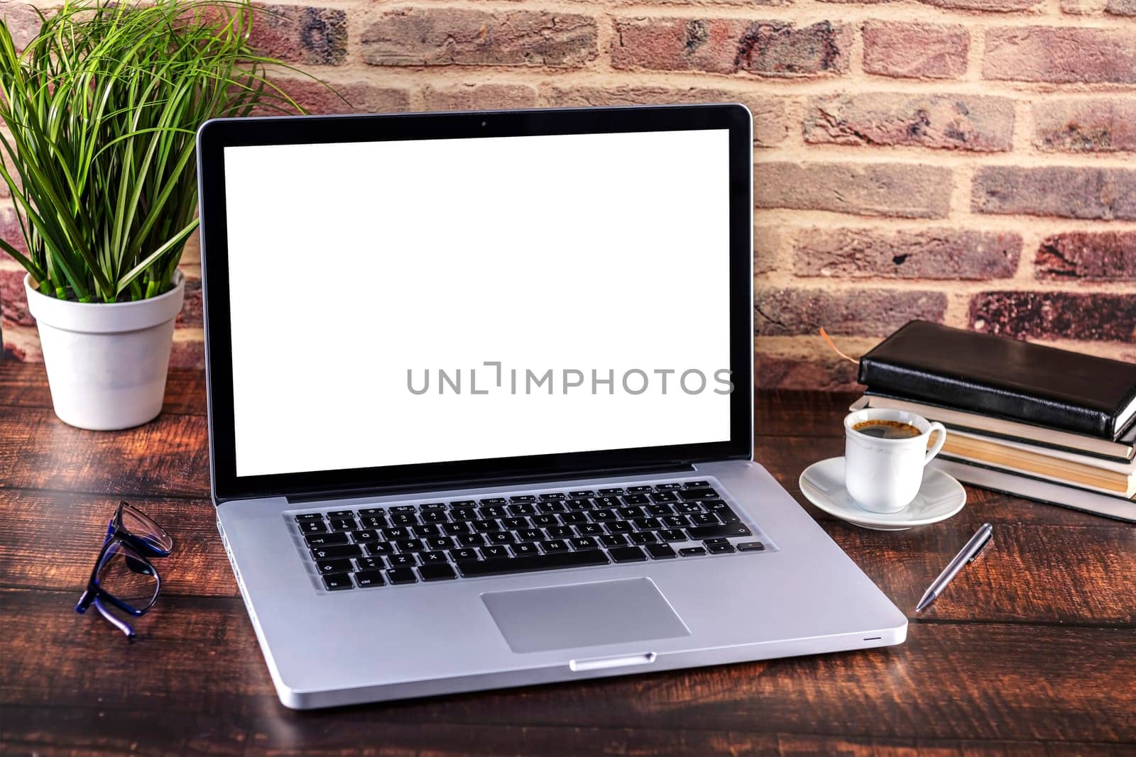 Laptop notebook with blank screen and cup of coffee and notepad pen and books and smart-phone on wooden table. Mock up on wooden table with laptop with blank screen, cup of coffee, pen, books and flower. Focus on keyboard.