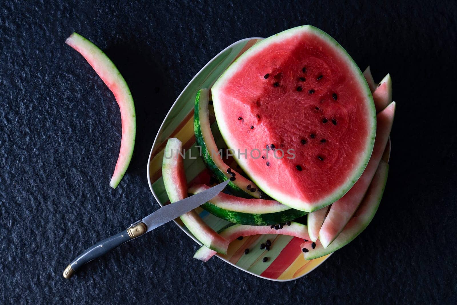 Piece of watermelon with cut slices and eaten on a plate with a knife on a black background